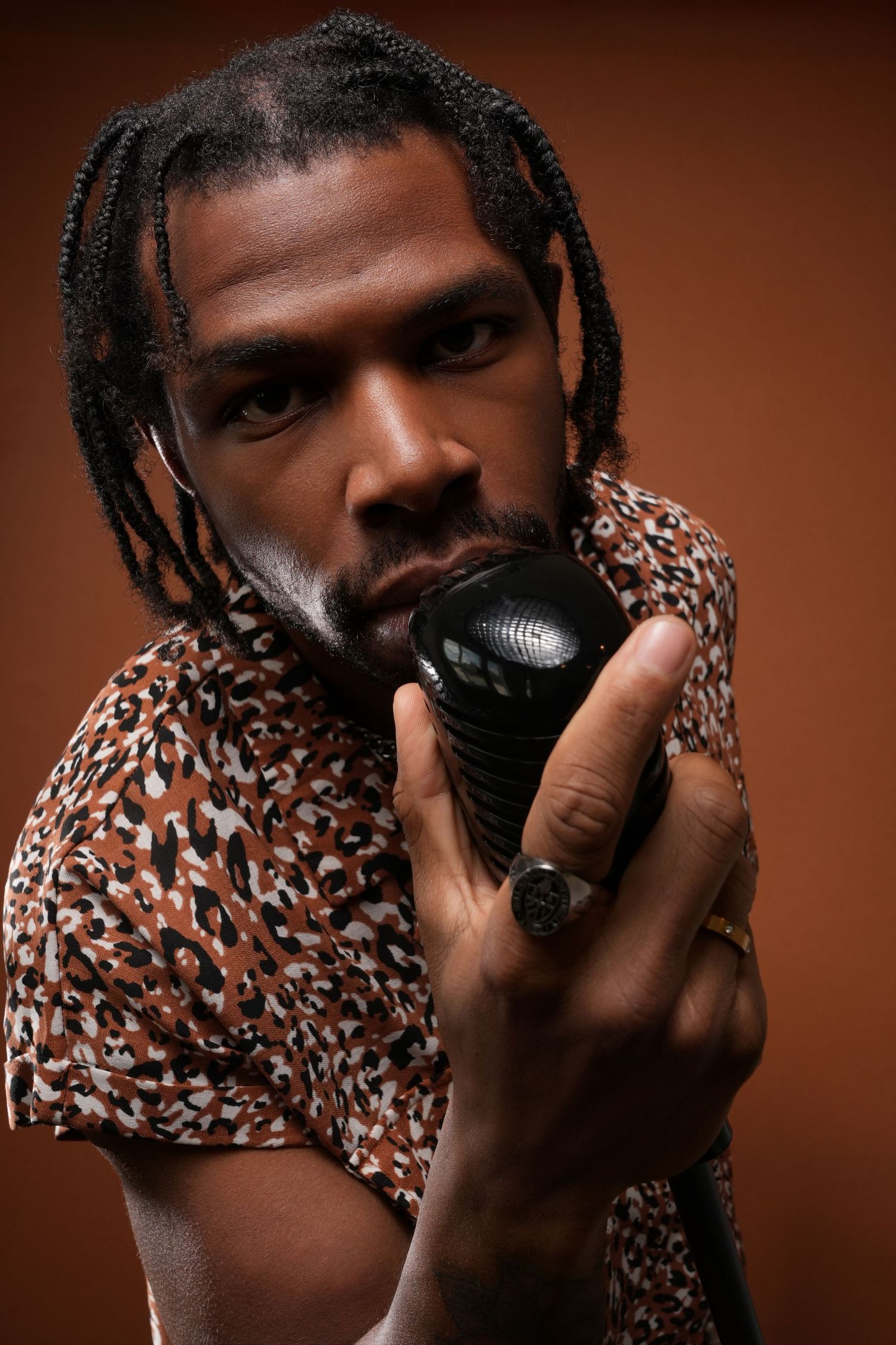 Dramatic portrait holding vintage microphone in animal print shirt against brown background.