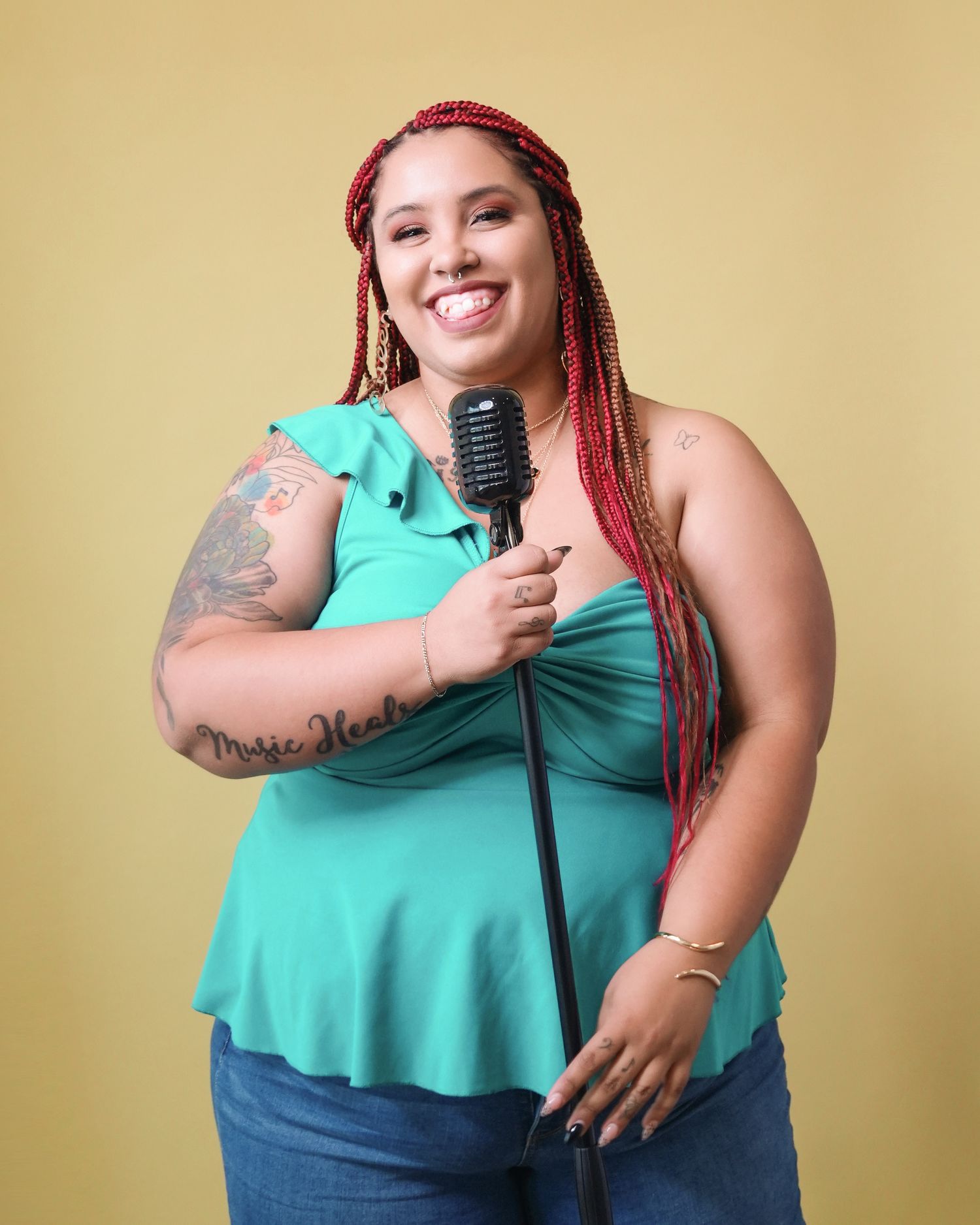 Performer in teal top holds vintage microphone against yellow backdrop.
