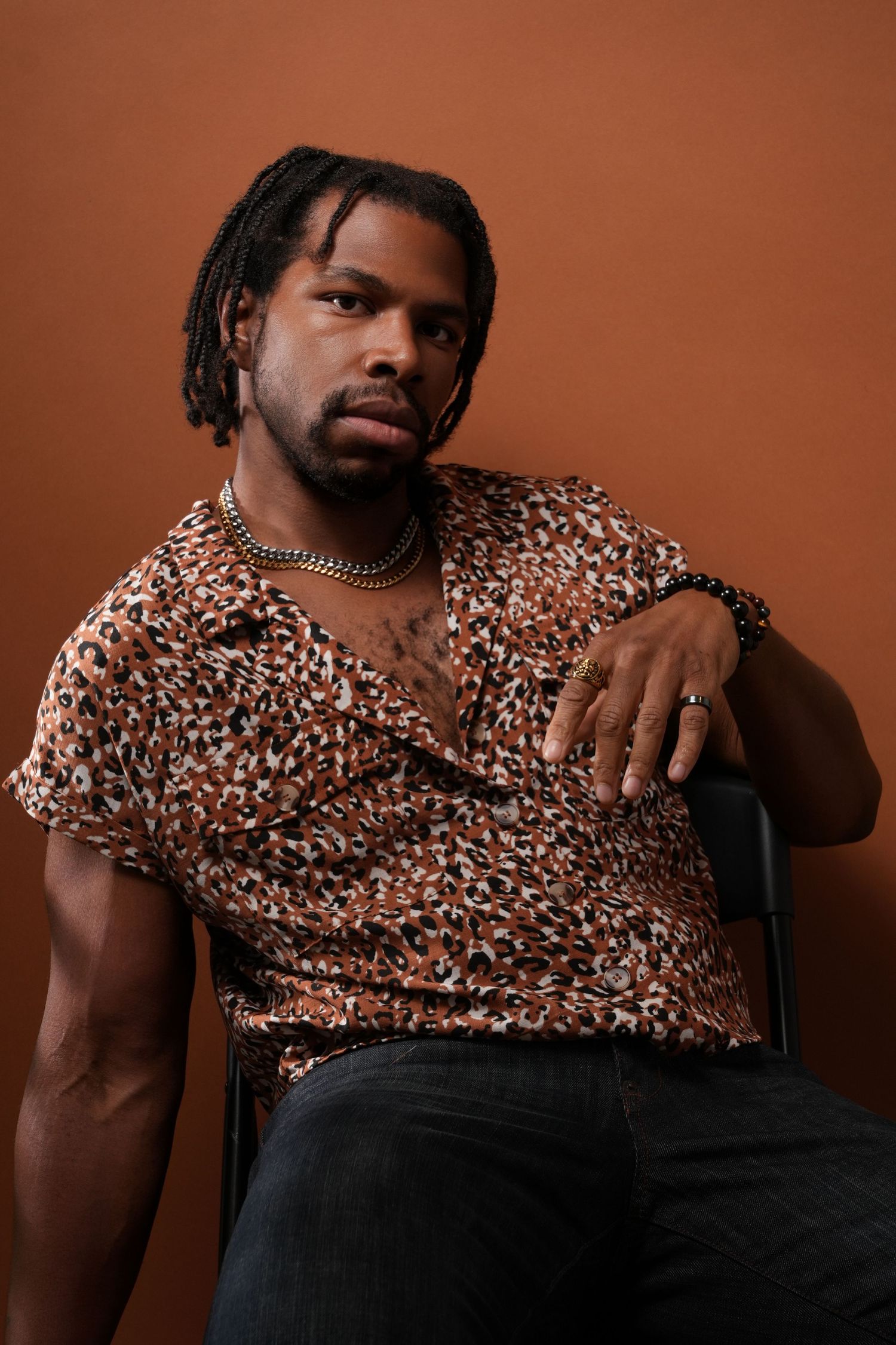 Stylish portrait in patterned short sleeve shirt sitting against warm brown backdrop.