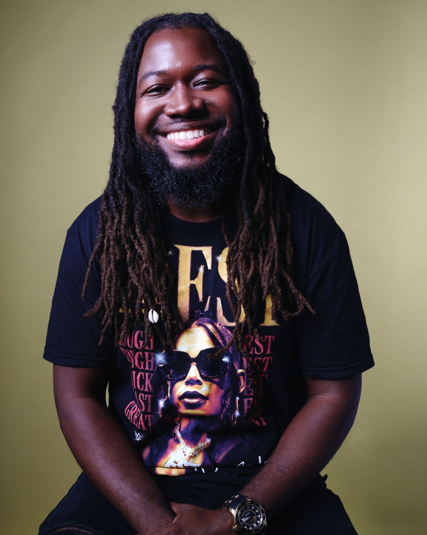 Person in graphic t-shirt smiles warmly while seated against neutral background.