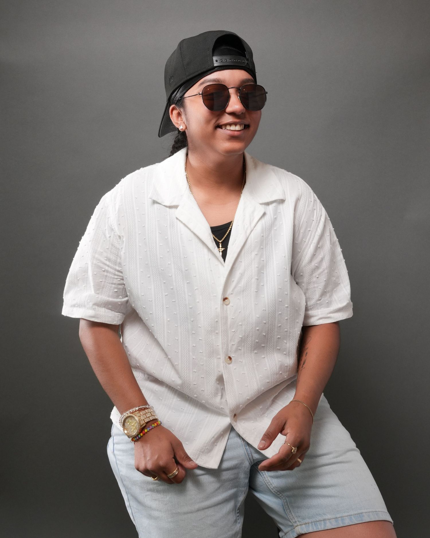 Casual studio portrait of a person in white button-down shirt, baseball cap and sunglasses.