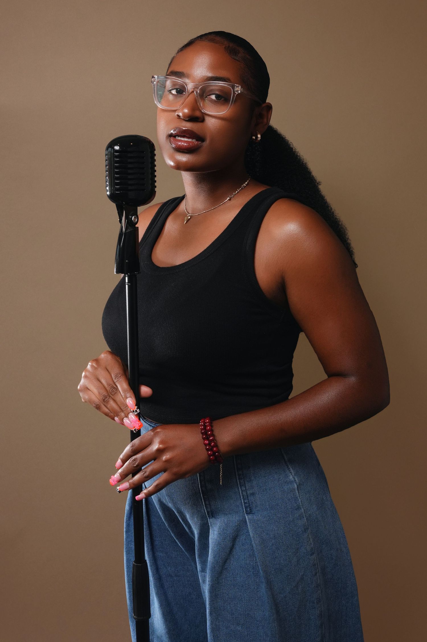 Studio portrait of a person in black tank top posing with vintage microphone against brown background.