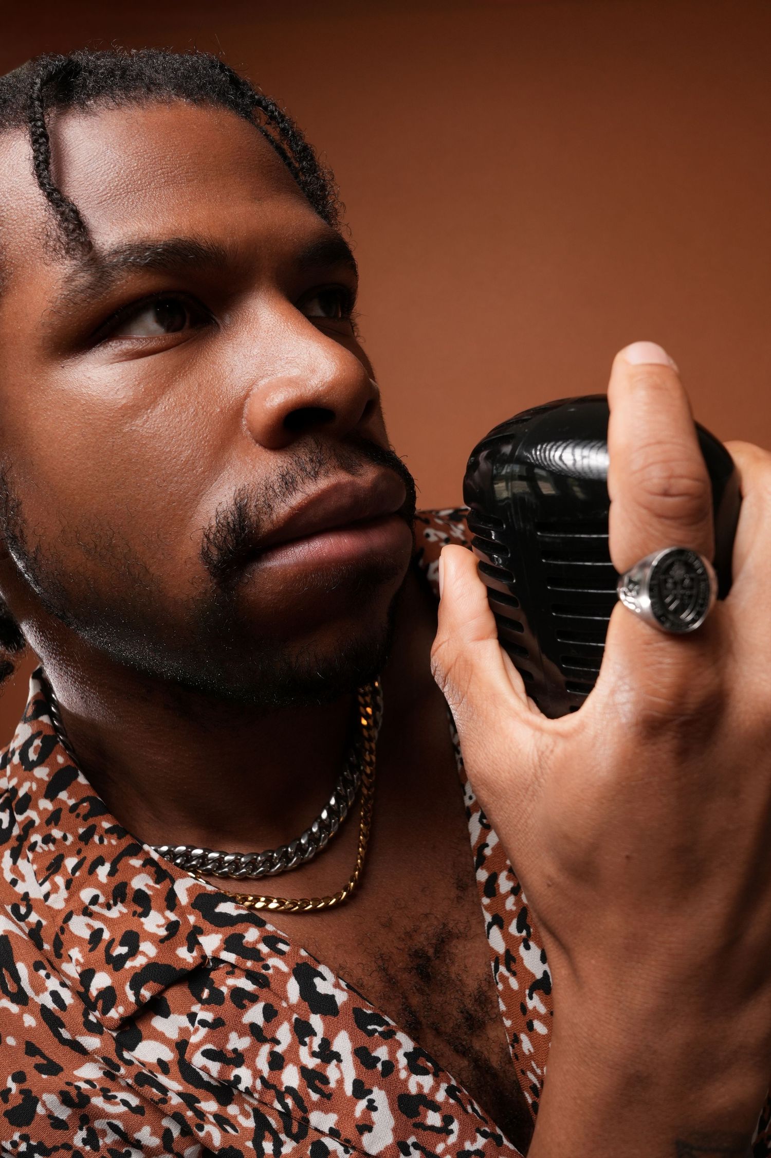 Close-up shot with vintage microphone and statement ring against brown background.
