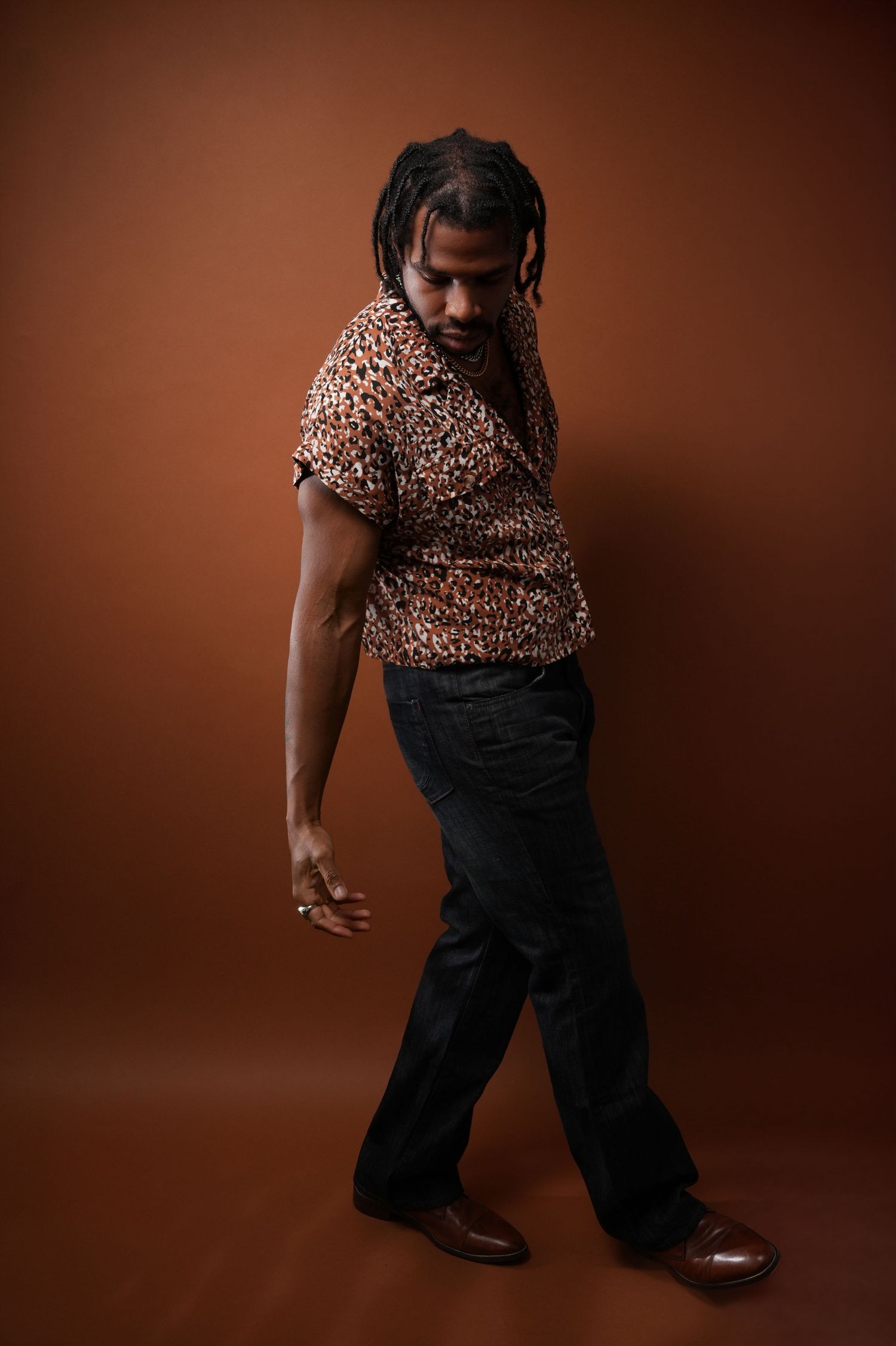 Full body fashion shot in leopard print shirt and dark pants against brown backdrop.