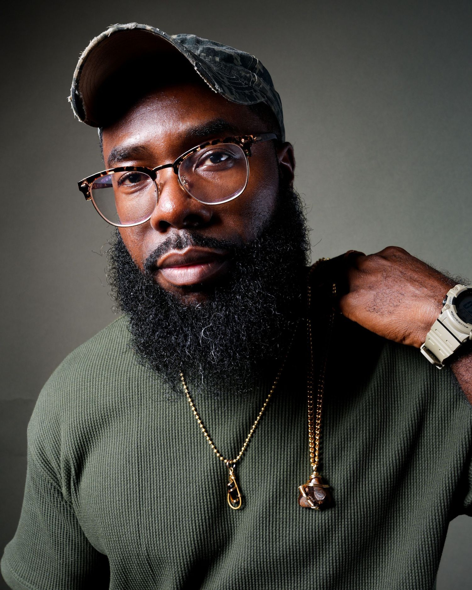 A series of portraits showing a person wearing a green sweater, glasses, and a full beard with gold chains as accessories.