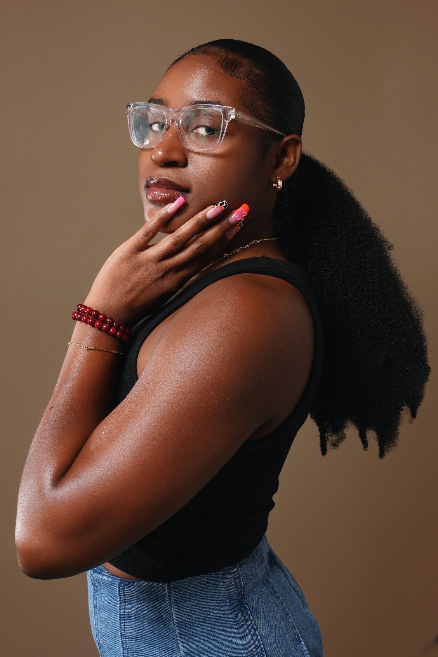 Artistic portrait of a person in glasses and black tank top posing with hand near face.