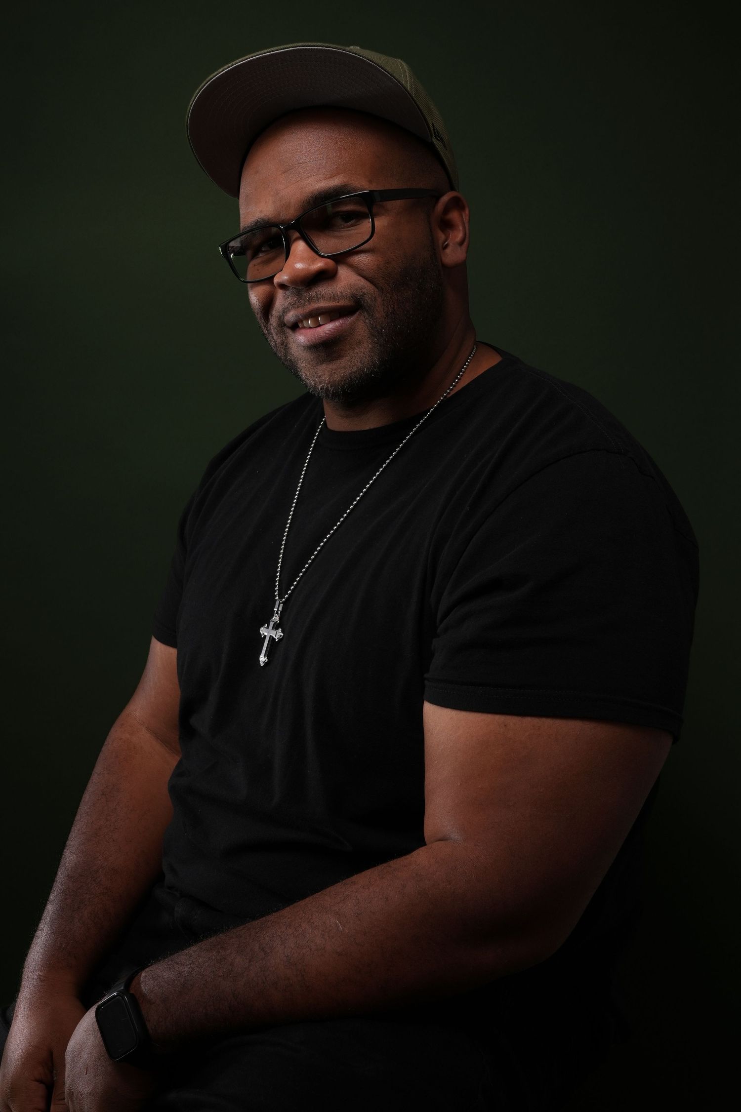 Portrait against dark green background wearing baseball cap and glasses.