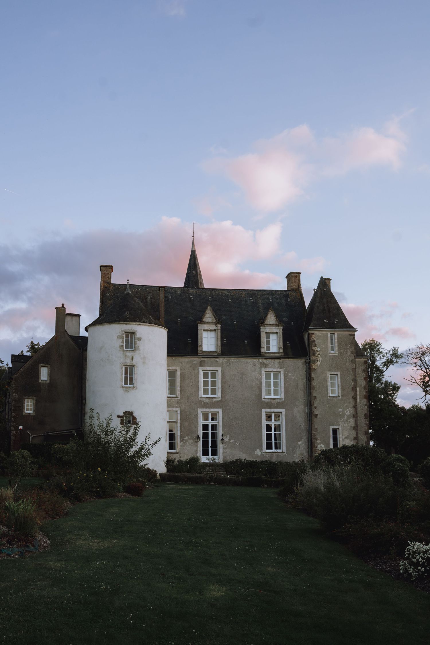 Historic stone mansion with white and gray exterior sits atop a grassy hill at dusk.