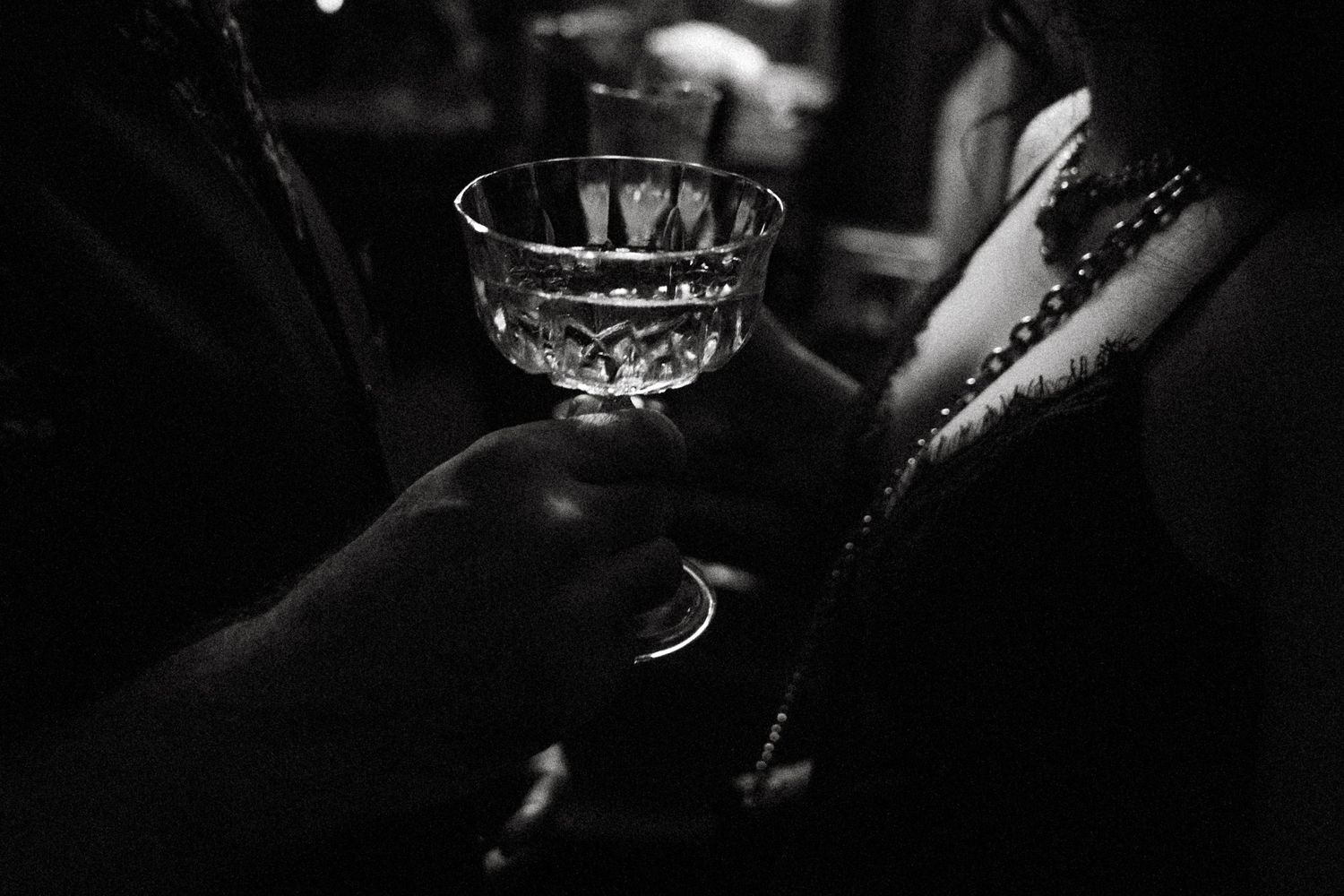 A close-up black and white photo shows hands holding a glass of whiskey with ice cubes.