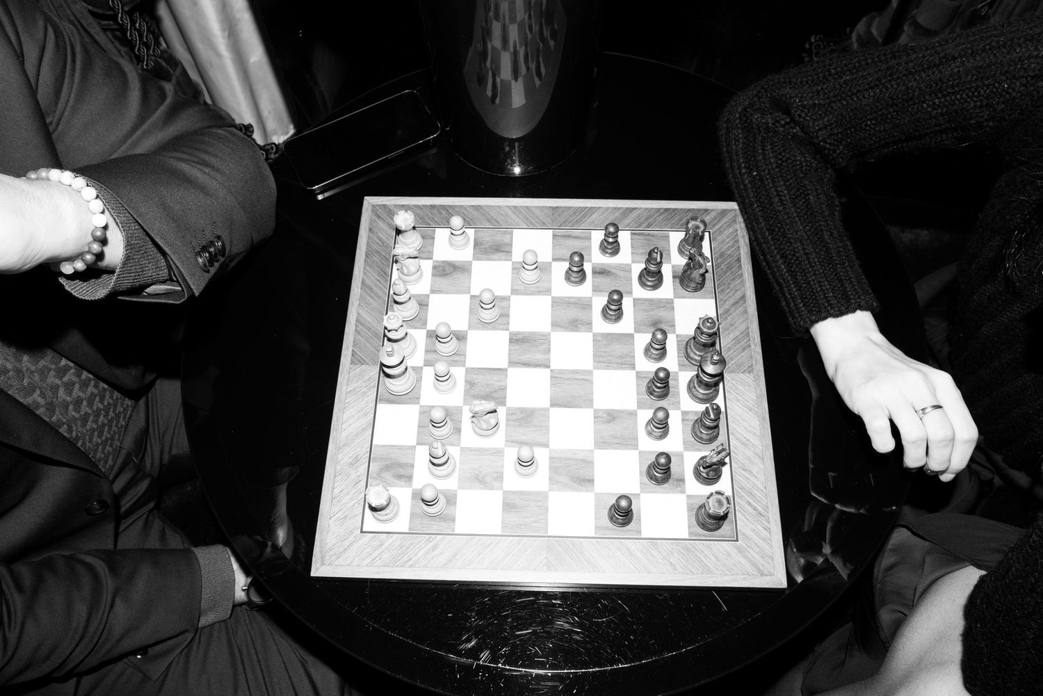 A sequence of six black and white photos showing hands moving chess pieces during a game on a chessboard.