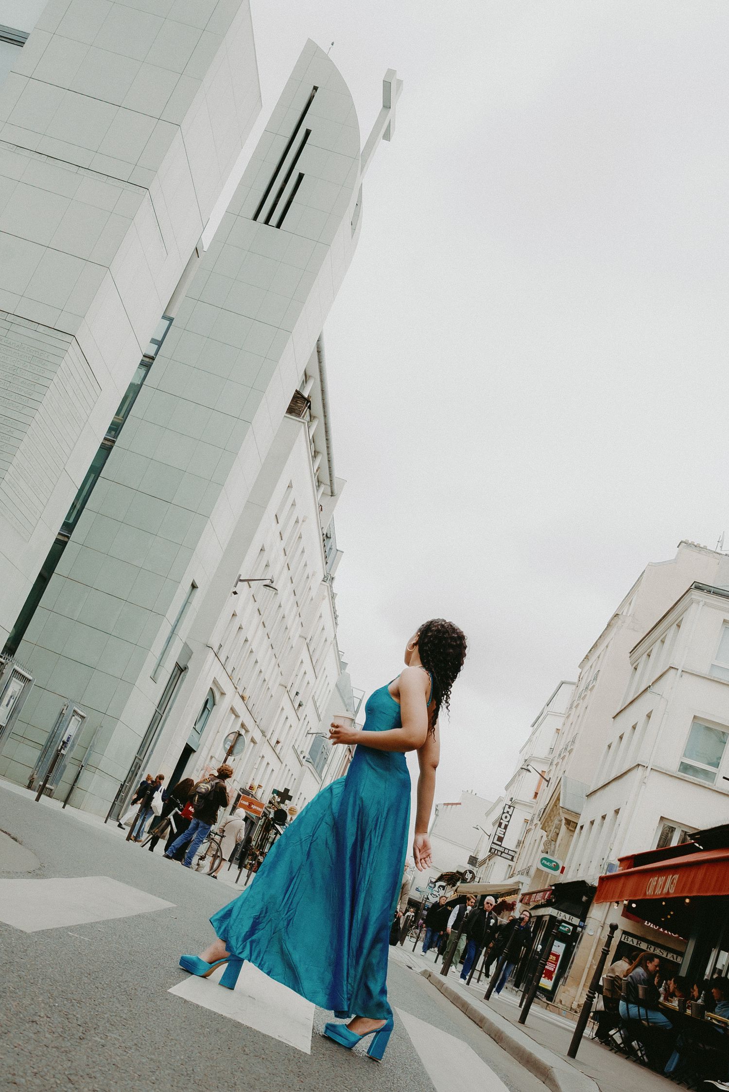 Editorial street style in Paris, bold turquoise dress in motion on a busy market street, cinematic and vibrant. Photo by Studio Reverie.