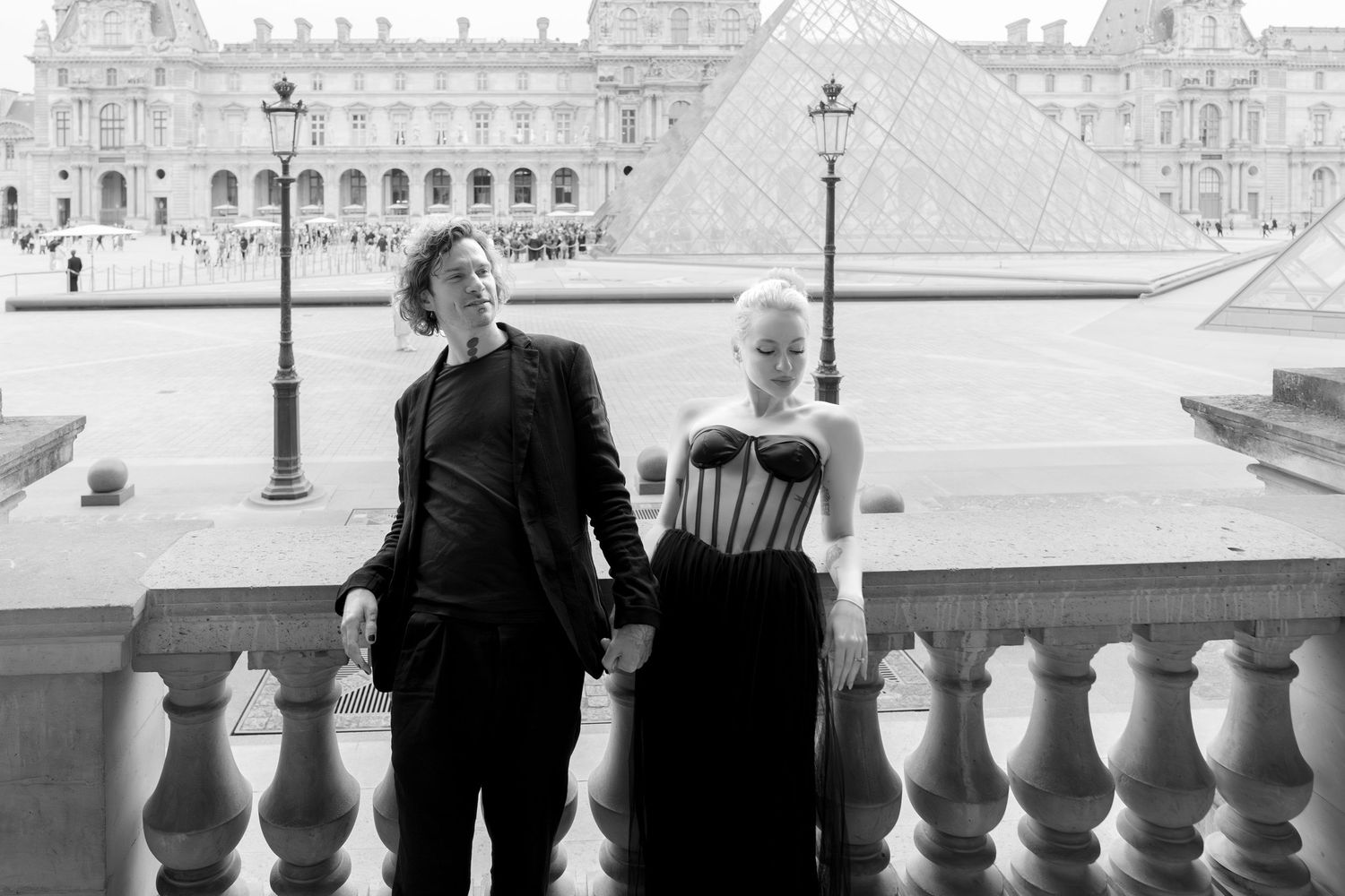Editorial couple holding hands in front of the Louvre Pyramid, Paris cinematic fashion-inspired photoshoot by Studio Reverie.