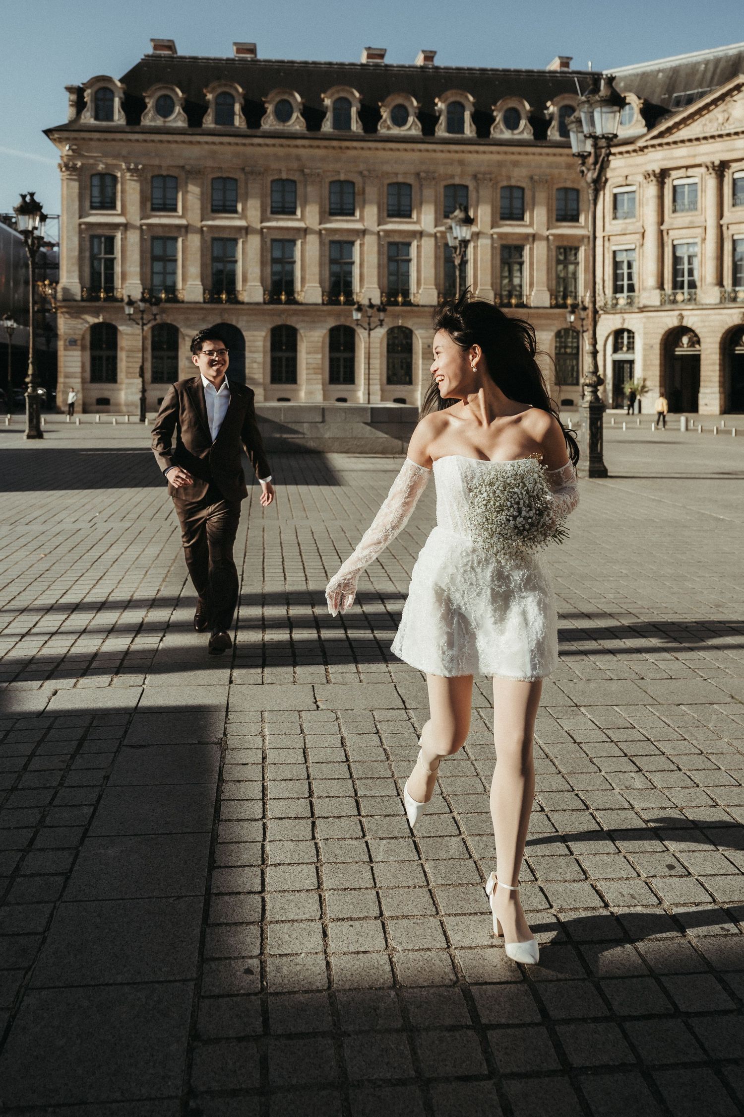 Joyful wedding couple runs and plays in front of majestic European palace.