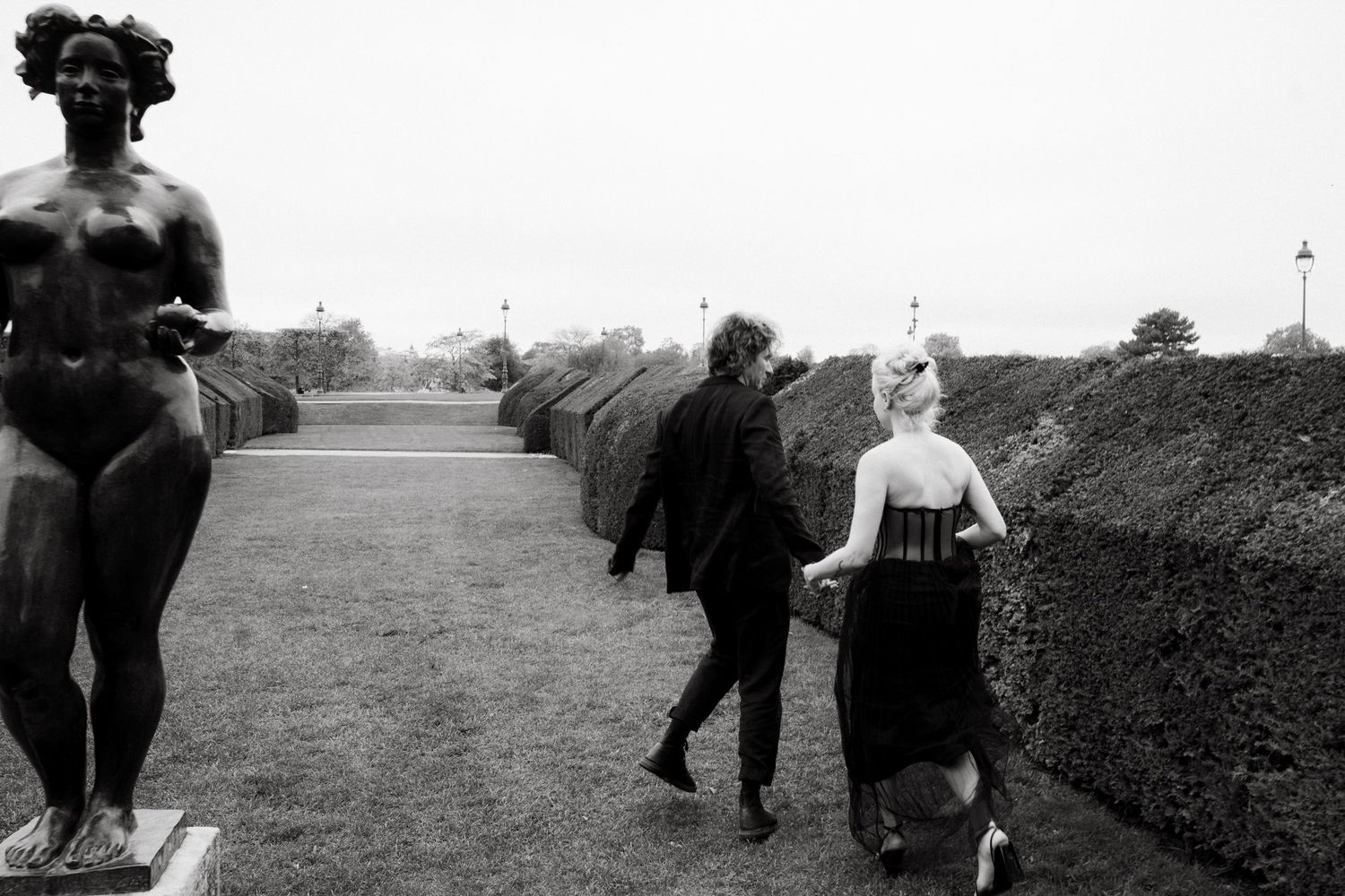 Couple walking hand in hand through Louvre sculpture gardens, Paris destination editorial photography by Studio Reverie.