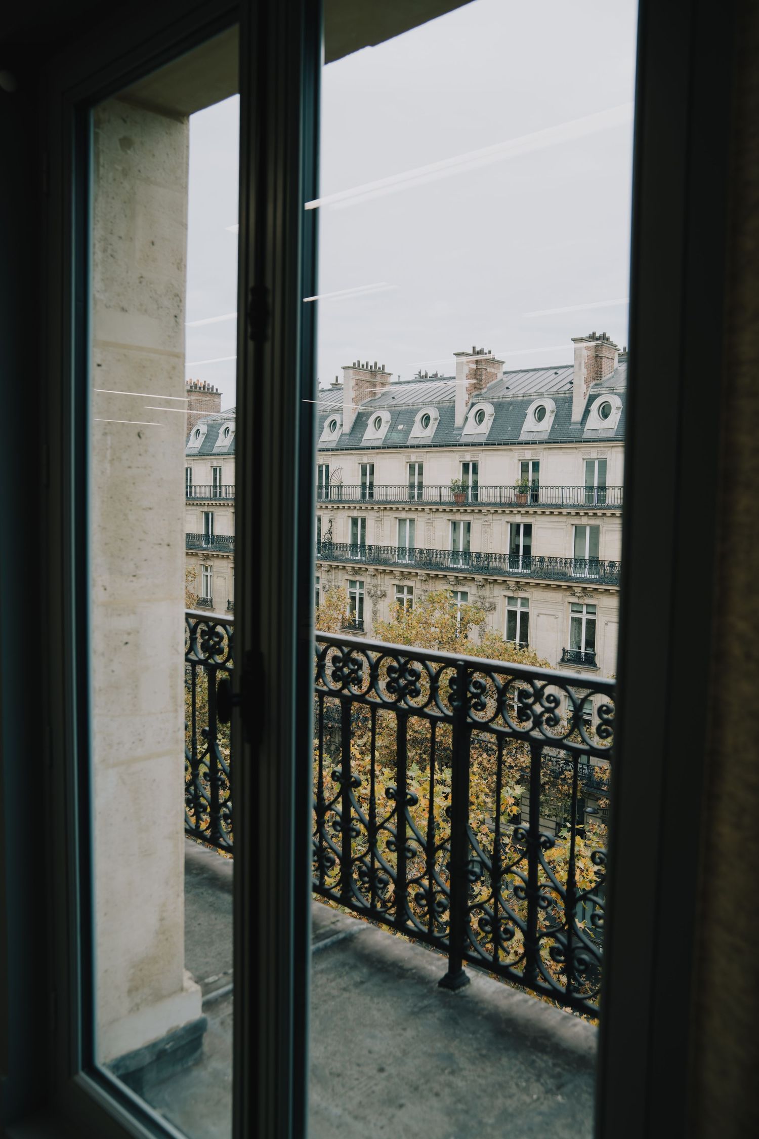 Atmospheric Paris event detail shot, soft daylight view through window to Haussmann rooftops, poetic and cinematic style