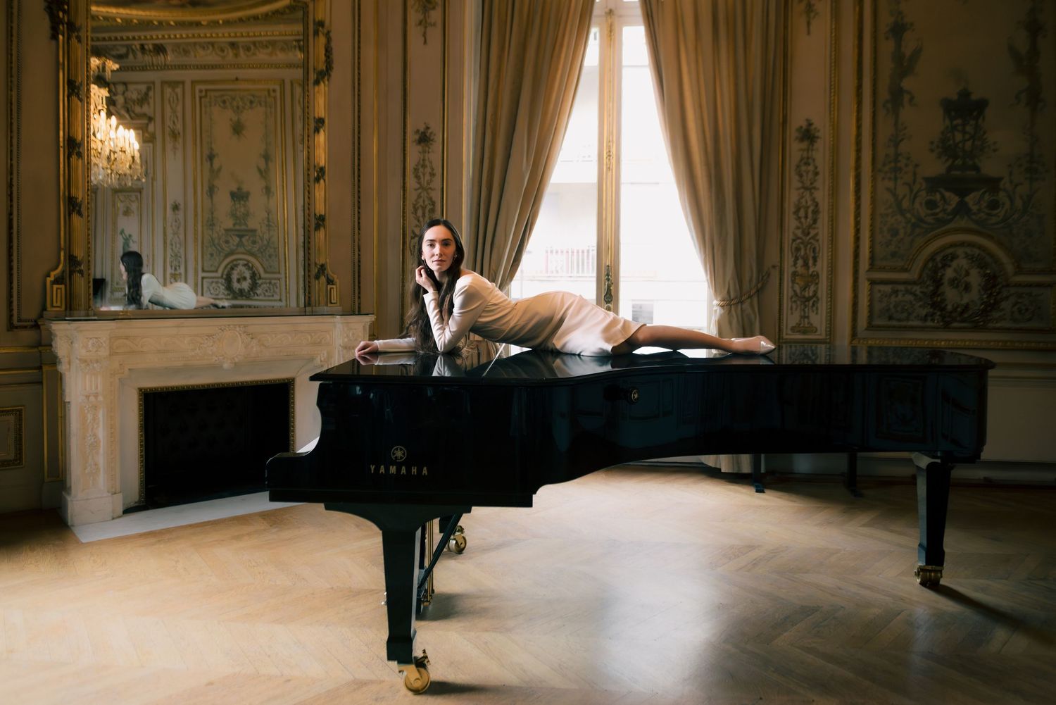 Elegant figure stands in a grand baroque palace ballroom with ornate gold details and dramatic lighting.