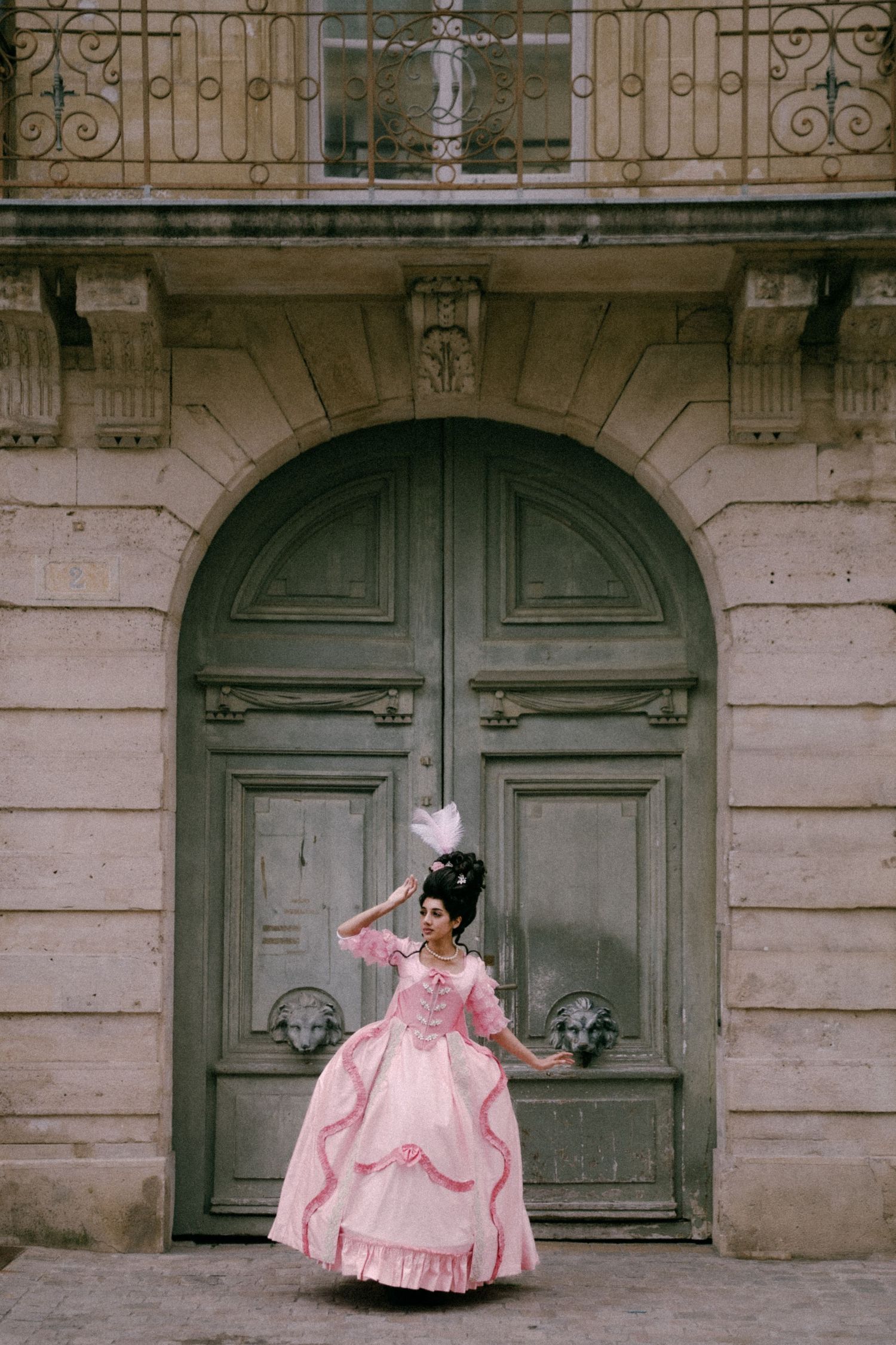 A pink rococo-style dress against a grand old European doorway with ornate architectural details.