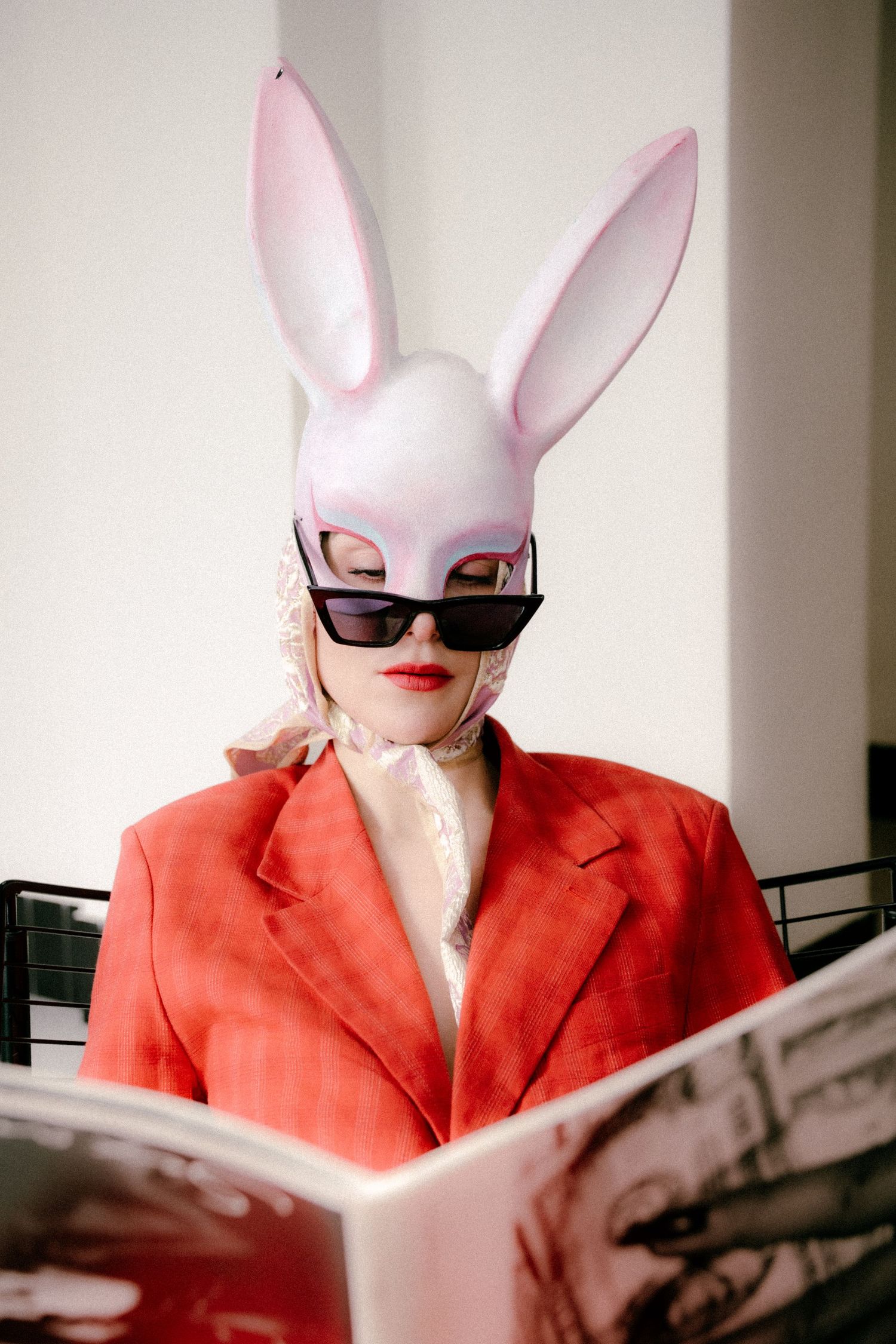 Whimsical Paris editorial with model in red suit and rabbit mask reading a newspaper, cinematic and surreal tone. Photo by Studio Reverie.