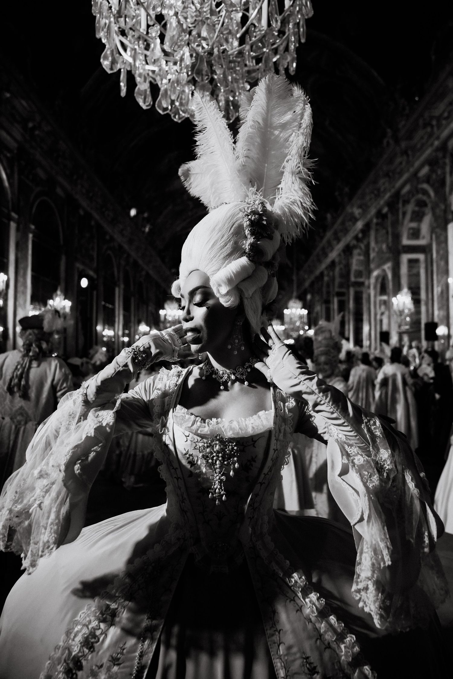 Performers in ornate period costumes and masks dance at a nighttime baroque celebration in the hall of mirrors at Versailles