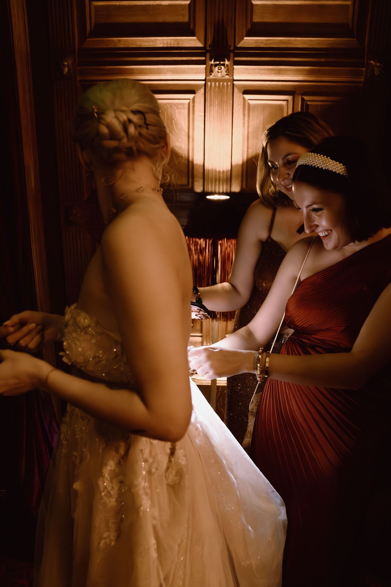 Candid moments of wedding preparation in warm sepia tones showing dress adjustments and final touches.