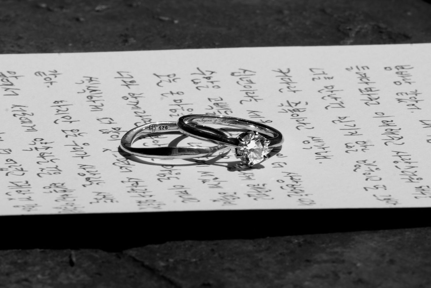 Handwritten text in black ink appears on a white paper with a dark background and a partial view of a metallic object.