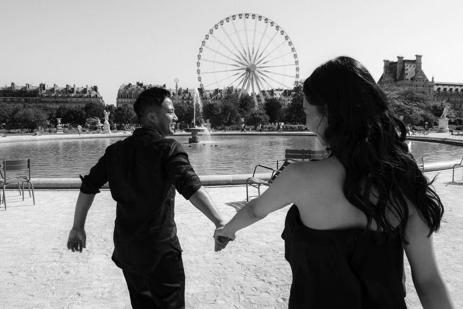 Cinematic couple holding hands at Jardin des Tuileries, Paris with Ferris wheel in background, black and white photography by Studio Reverie