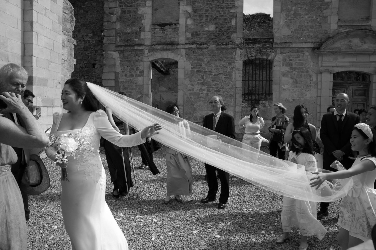 Wedding scene with a long flowing veil caught in the wind against stone architecture.