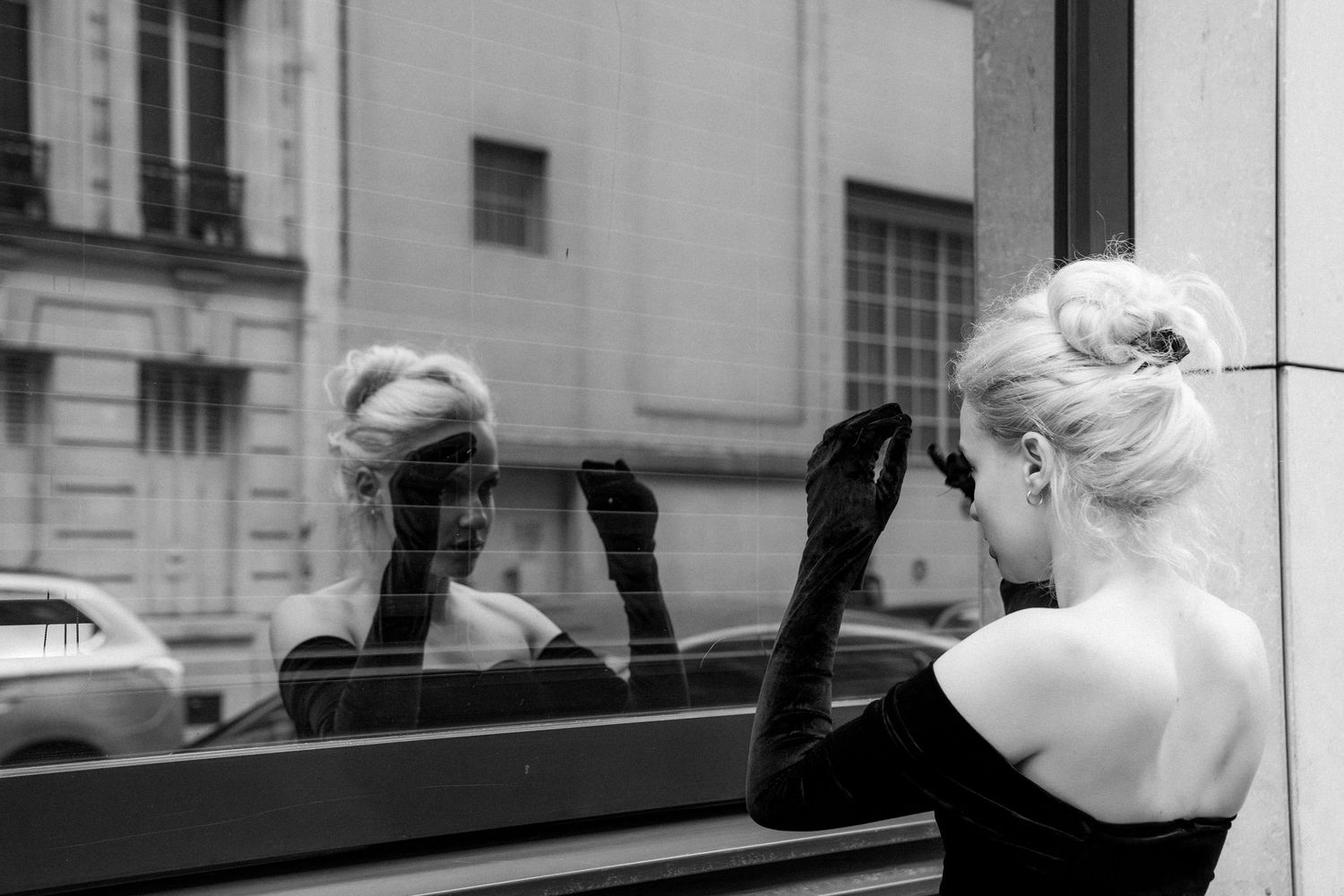Woman in black velvet gloves and off-shoulder dress, reflected in glass near Louvre, Paris fashion editorial by Studio Reverie.