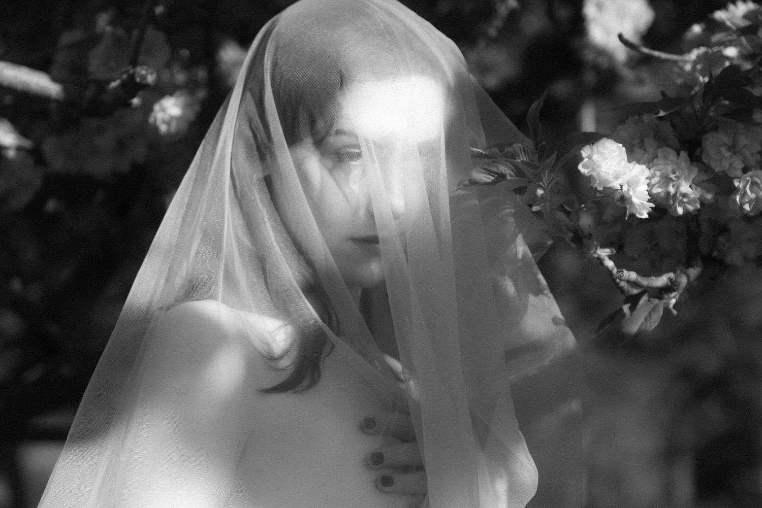A moody black and white photo shows a figure behind a translucent veil creating an ethereal, dreamy effect.