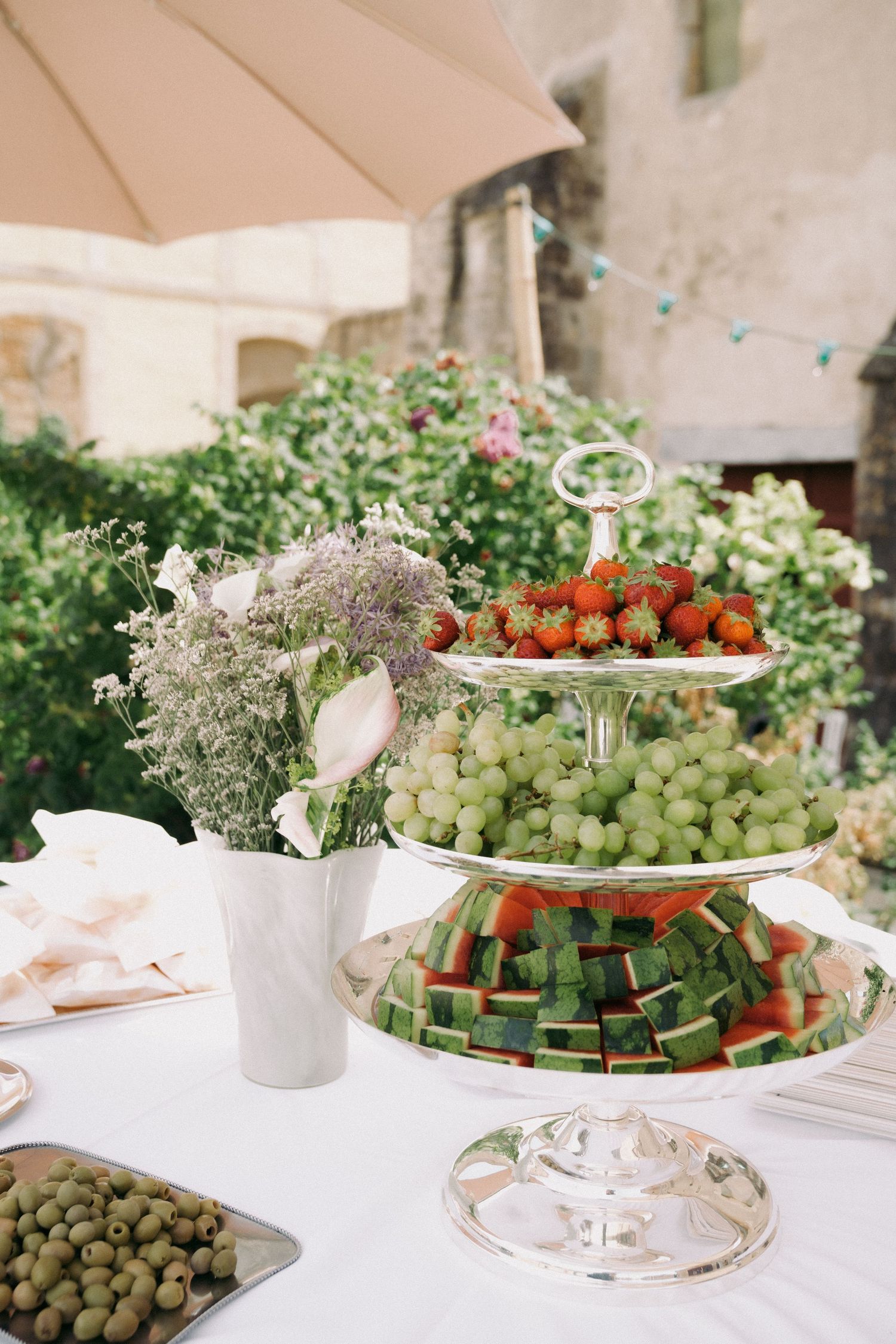 Elegant tiered serving platters display fresh fruits, vegetables and appetizers at an upscale catered event.