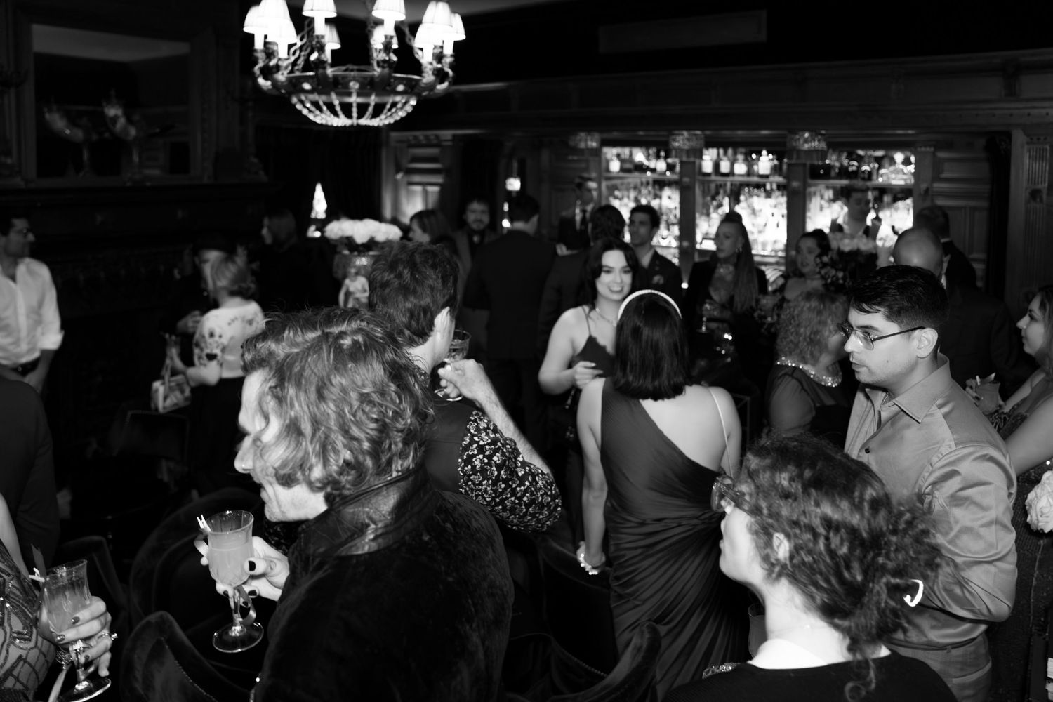 Dark nightclub scene with crowd of people dancing and socializing under dim lighting.