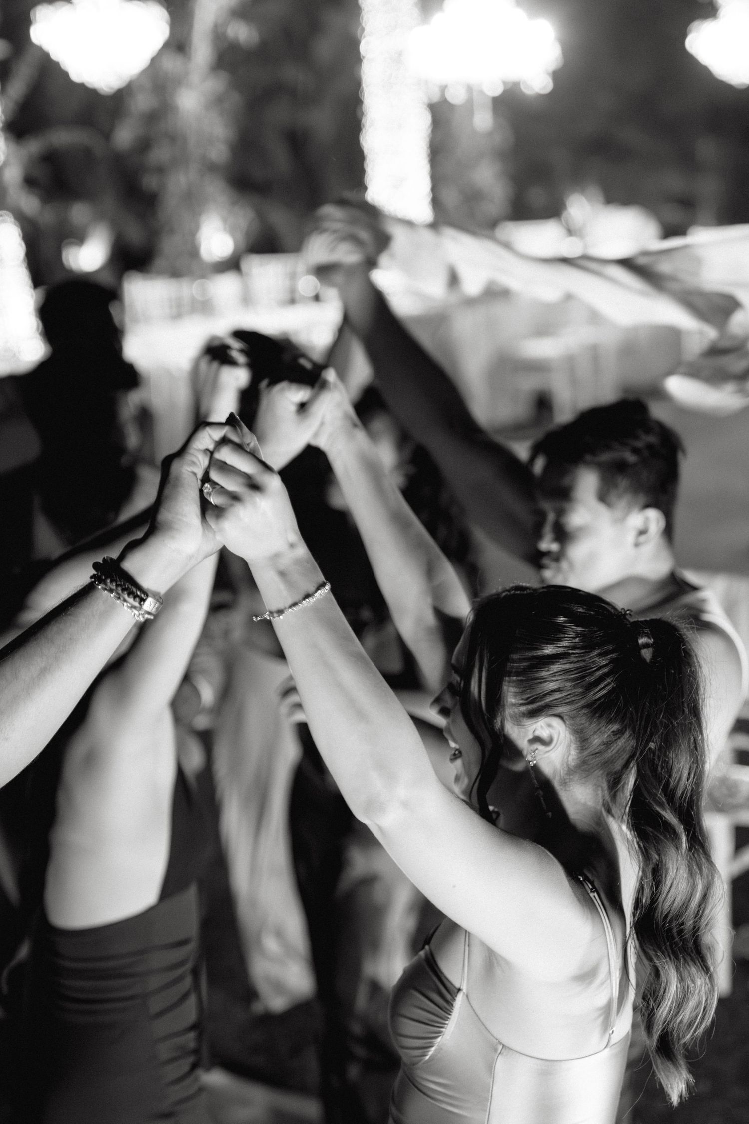 People dancing with raised arms in silhouette against a dark background at an outdoor event.