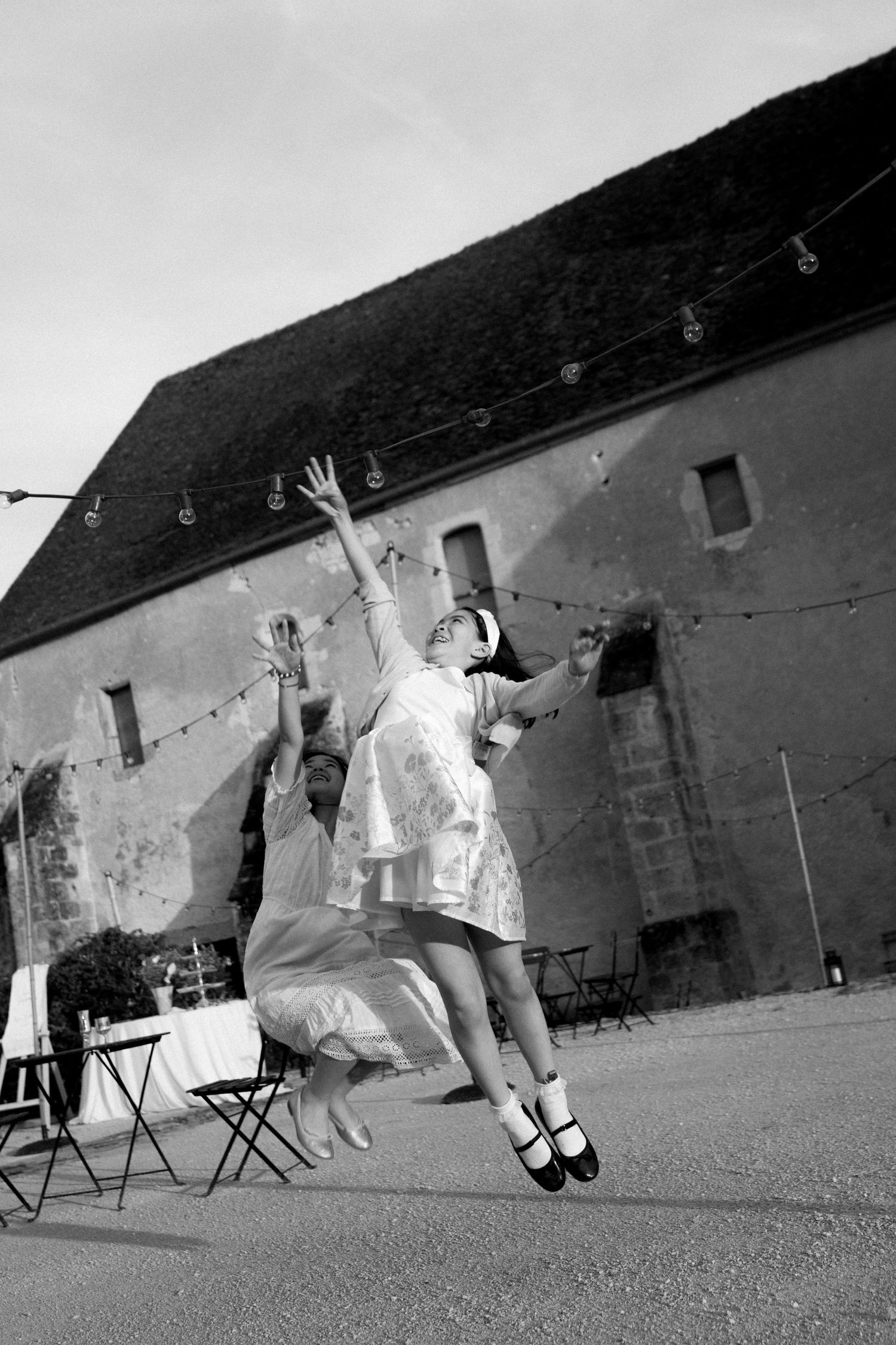 Sequence of joyful wedding guests jumping in front of a rustic barn wall with string lights.