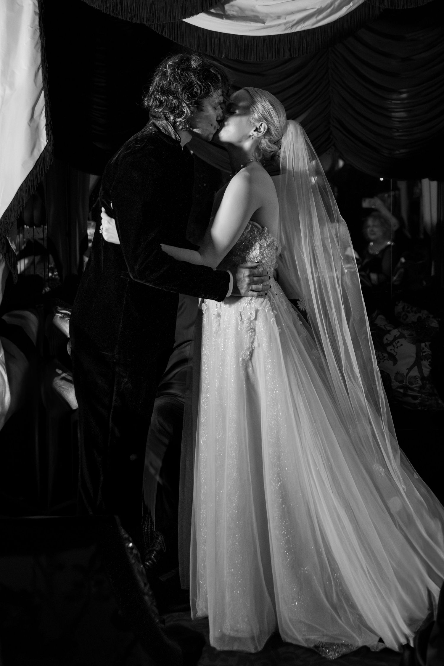A couple shares a romantic dance at their wedding reception in a dimly lit ballroom with flowing white gown and veil.