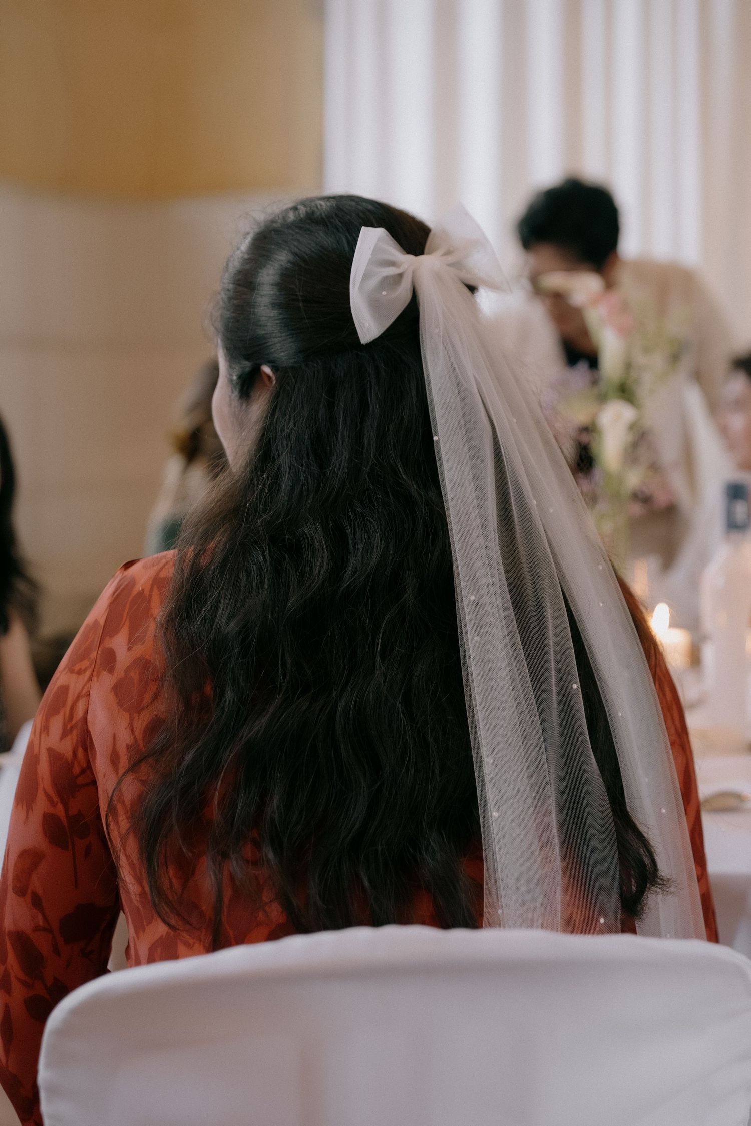 A wedding guest with long dark hair wears a white bow veil attachment.