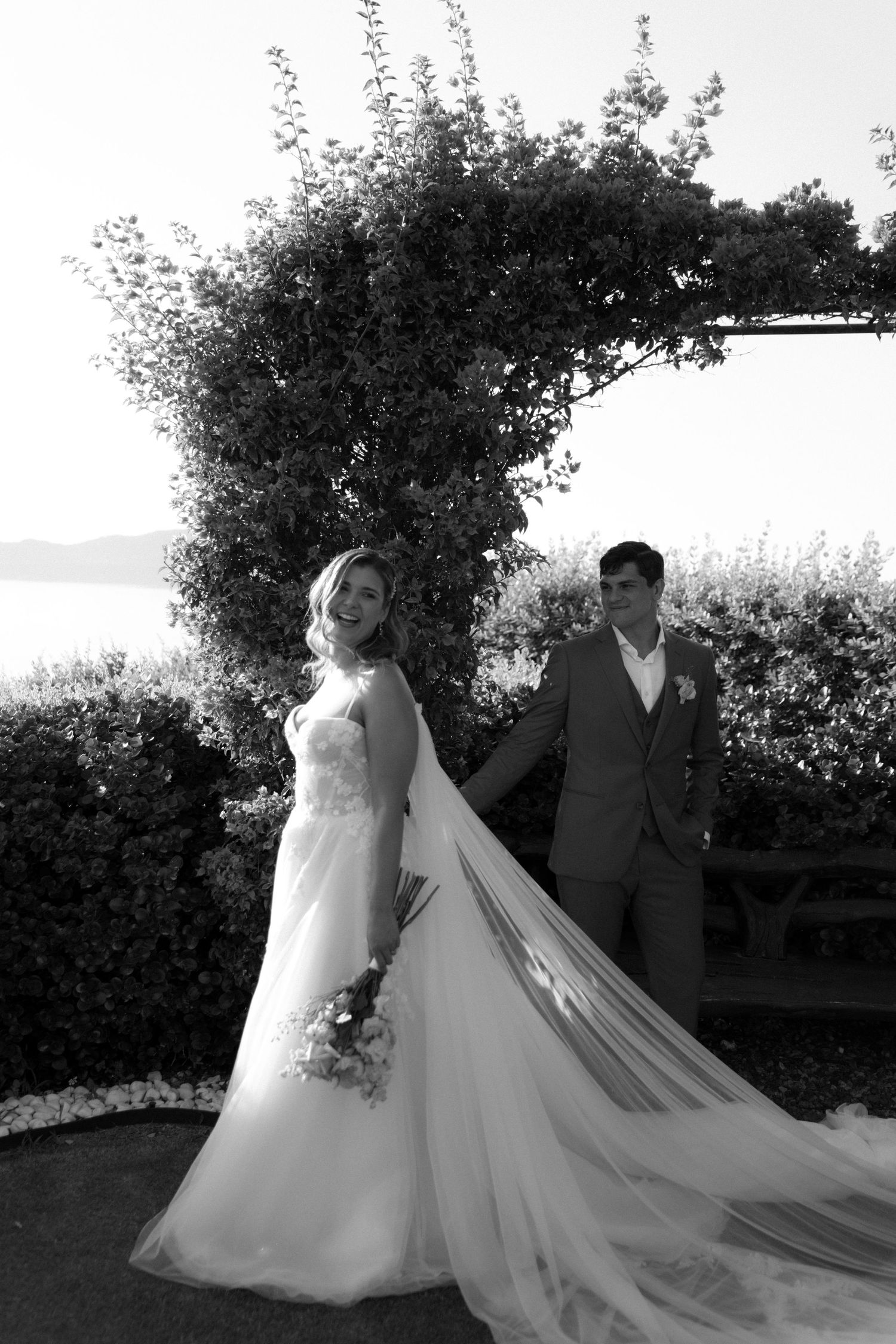 Wedding couple photographed in silhouette against a garden backdrop with flowing veil.