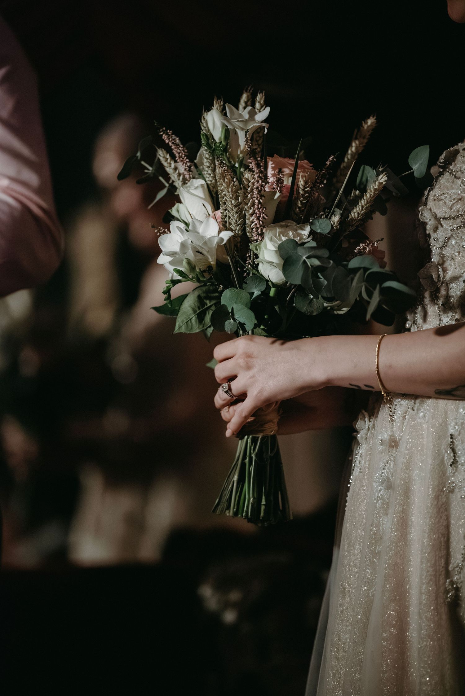 Close-up of white and green floral wedding bouquet with sparkly dress detail.