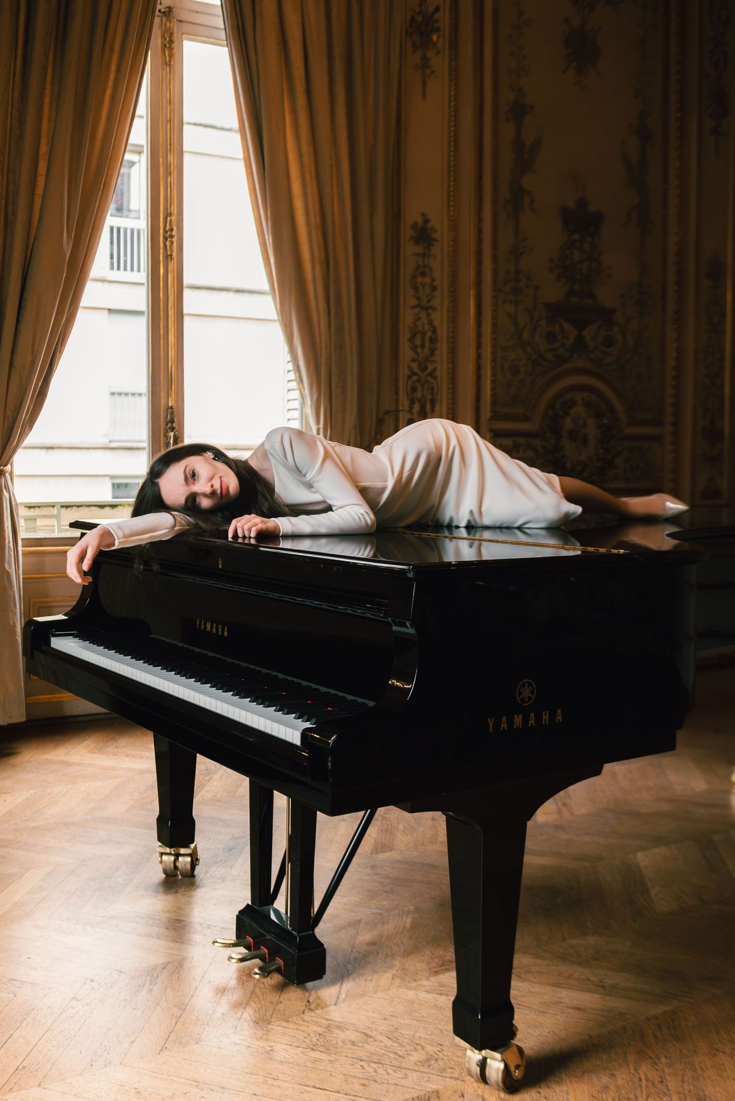 Four artistic photos of a grand piano in an elegant room with hardwood floors and golden curtains show different angles.