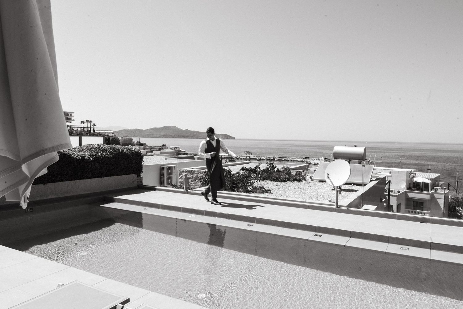 Wedding party stands in silhouette against bright sky on a modern rooftop terrace.