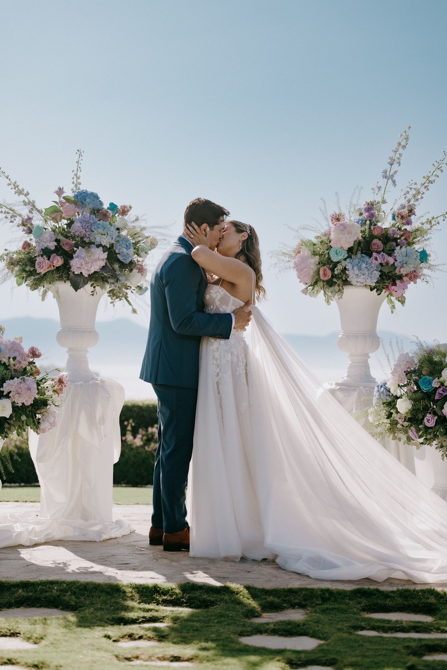 Elegant outdoor wedding ceremony setup with white floral arrangements and a couple sharing a romantic moment.