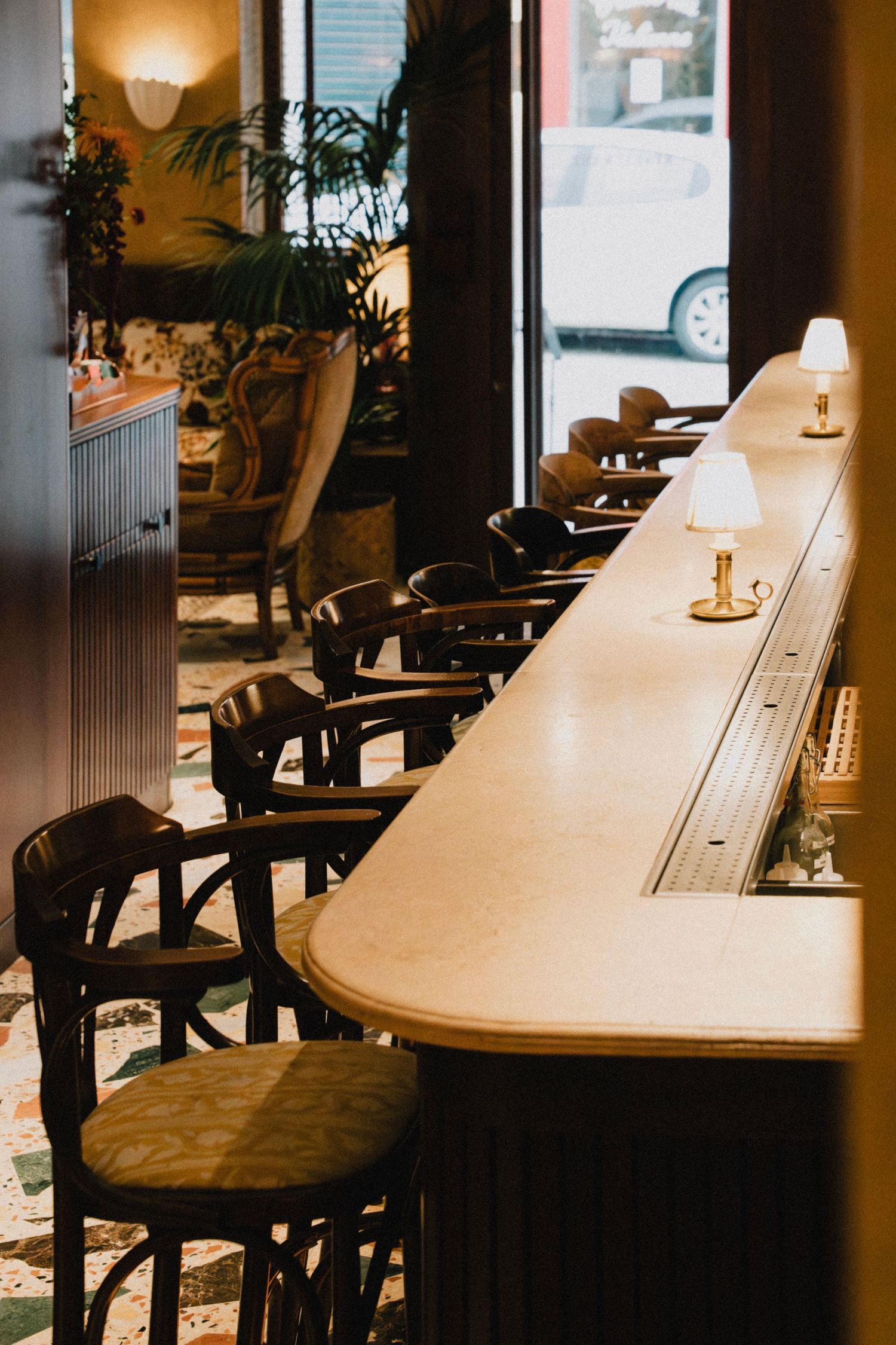 Vintage bar counter with dark wooden stools and warm lighting from small table lamps creating cozy ambiance.