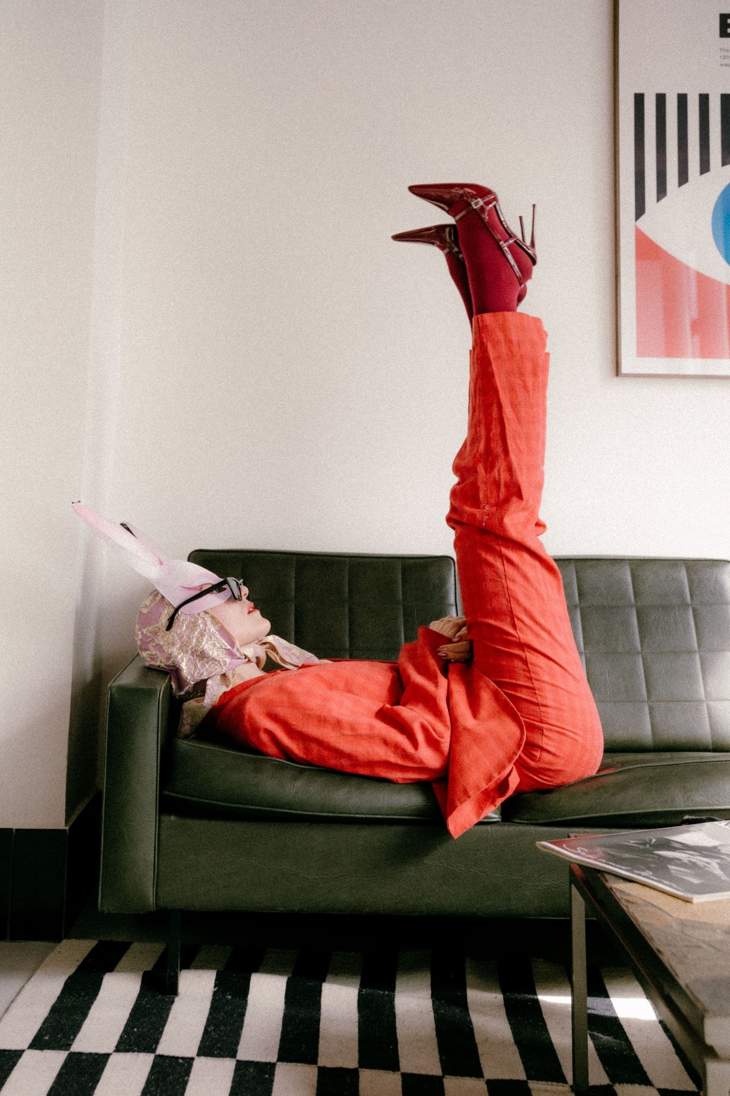 Editorial fashion portrait in Paris with model in red suit and heels, playful pose on mid-century green sofa.