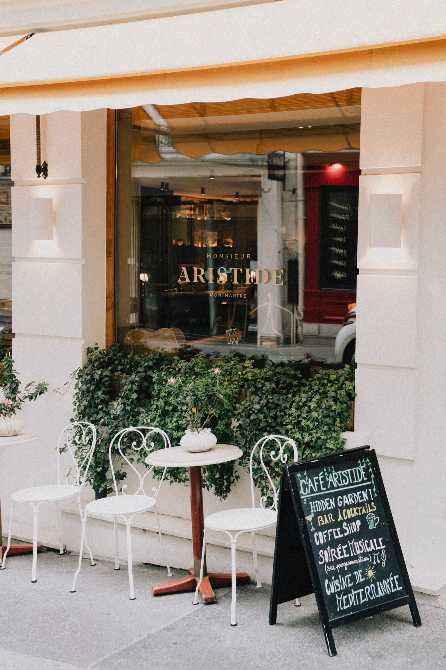 Charming Parisian cafe storefront with white metal chairs and blackboard menu on the sidewalk.