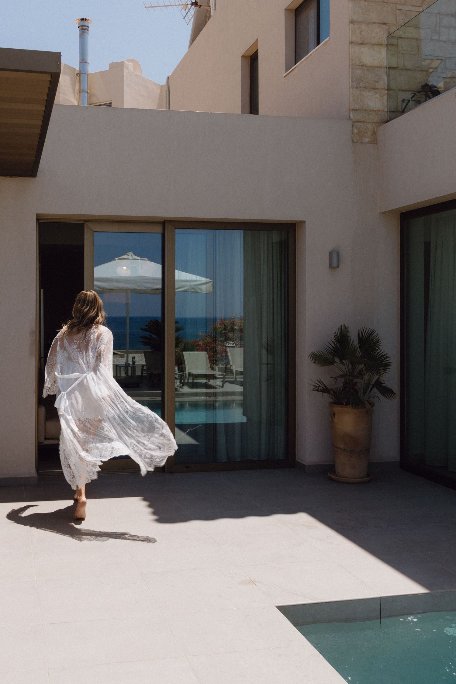 Ethereal bridal portrait with flowing white dress against modern architecture and pool.