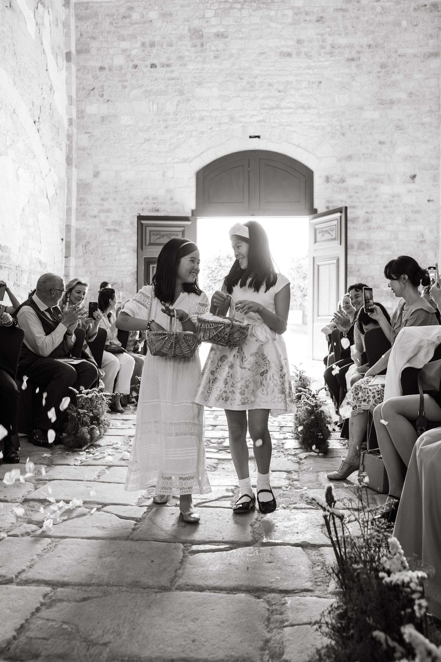 Wedding ceremony in a rustic stone venue with guests seated along a flower-lined aisle.