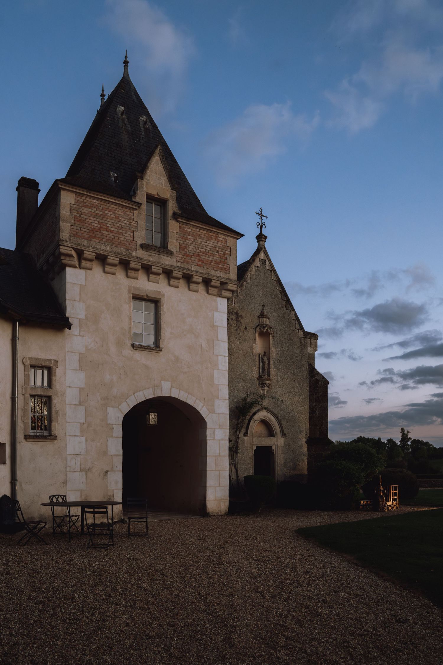 Historic stone chapel buildings with pointed roofs and arched doorways stand against a dusky blue sky at twilight.