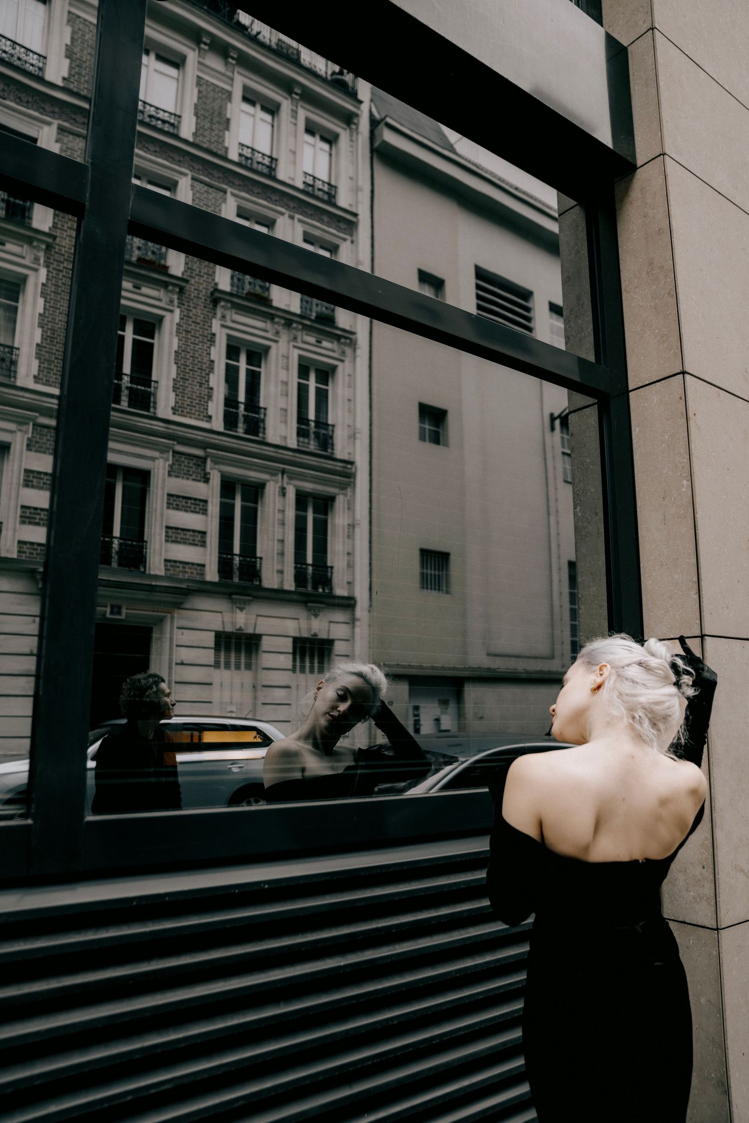 Editorial portrait in Paris with model in black dress reflected in city window, fashion-inspired photography by Studio Reverie.