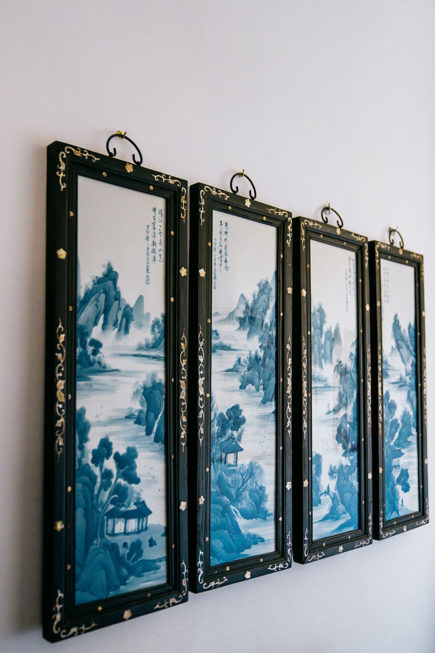Set of four traditional Chinese landscape paintings in blue and white displayed in ornate black frames on a wall.