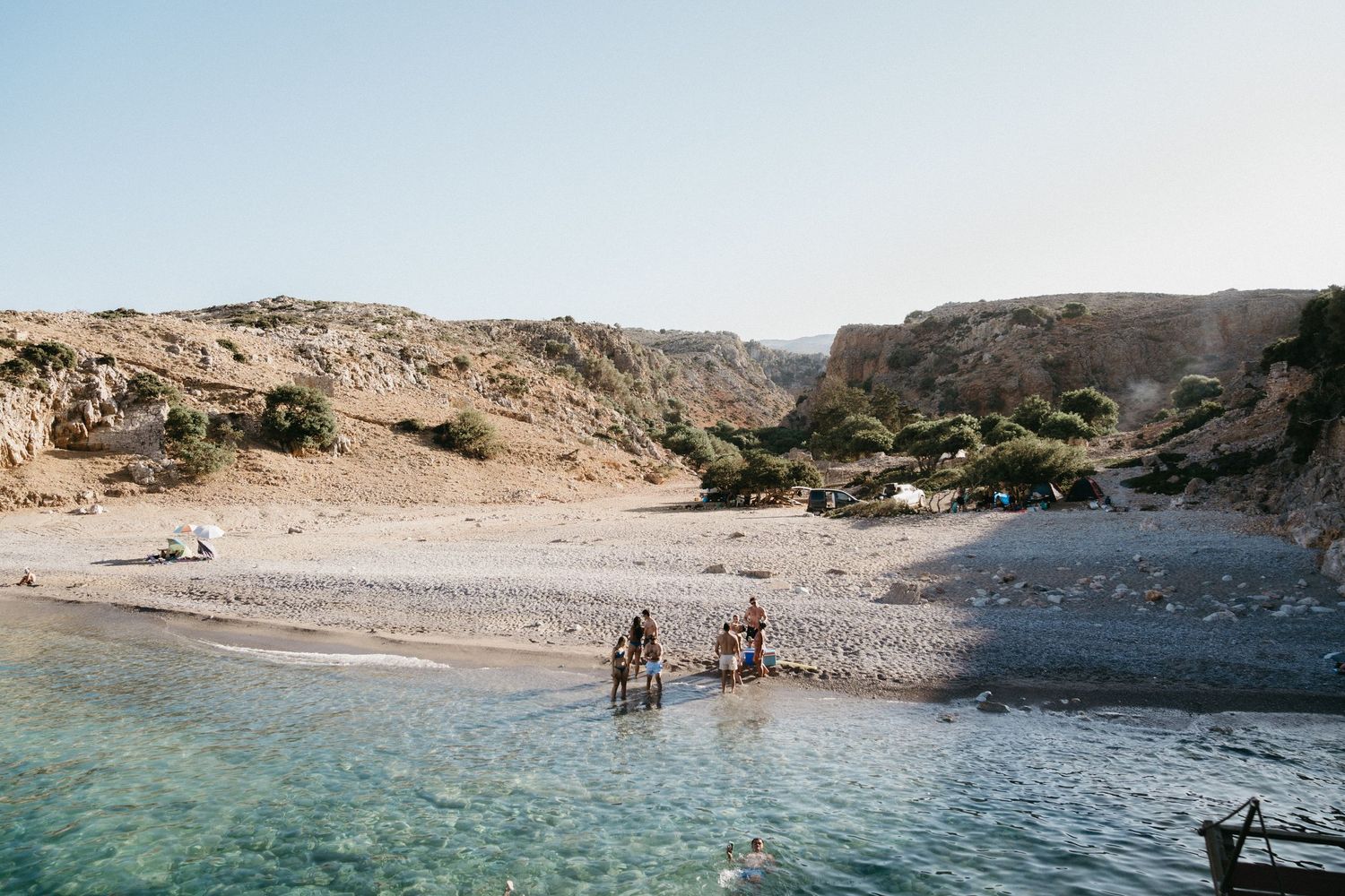 People enjoying a secluded beach cove with turquoise waters and rocky cliffs in a remote coastal landscape.