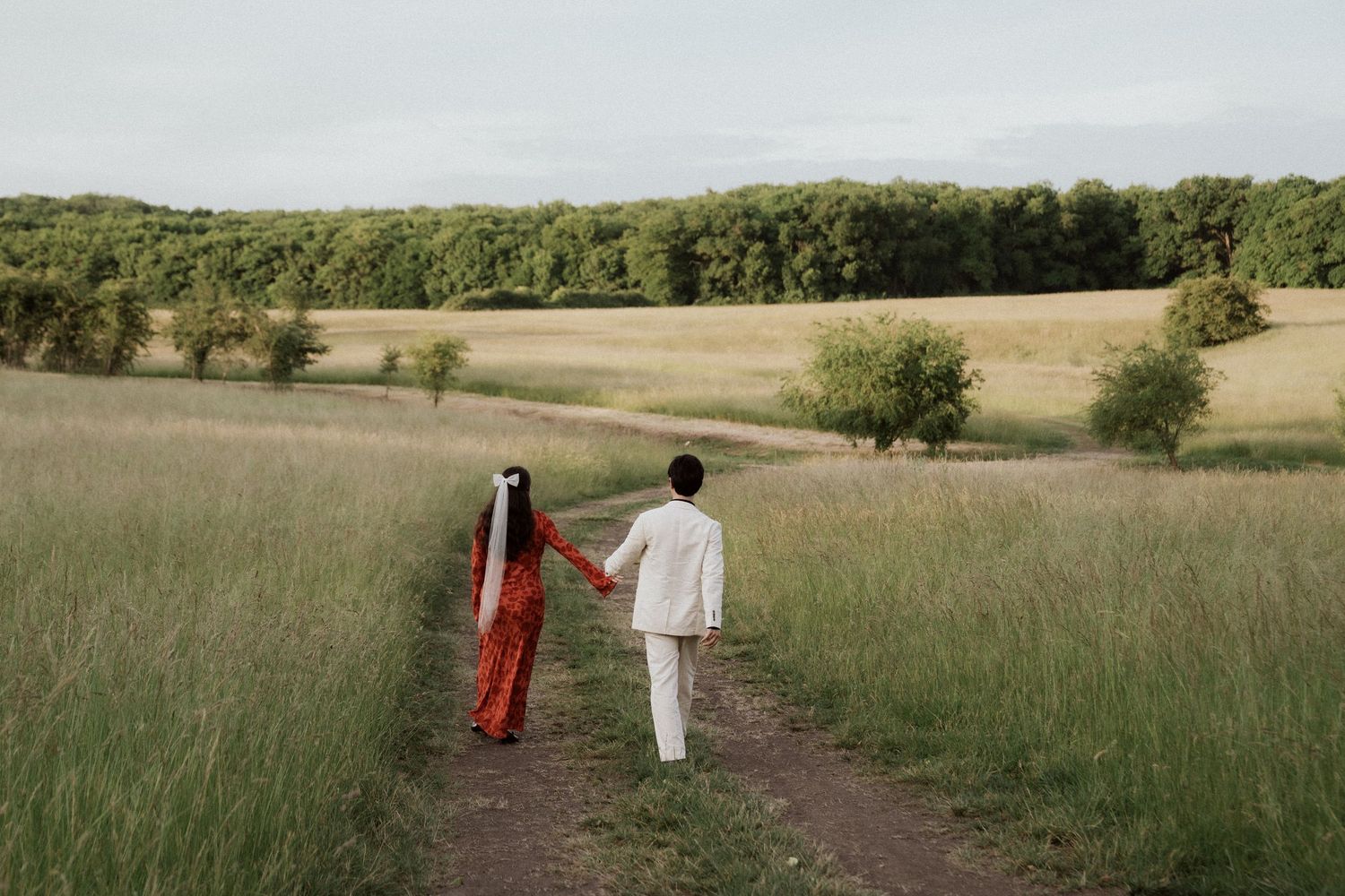 Two people walking along a dirt path through an open prairie landscape.